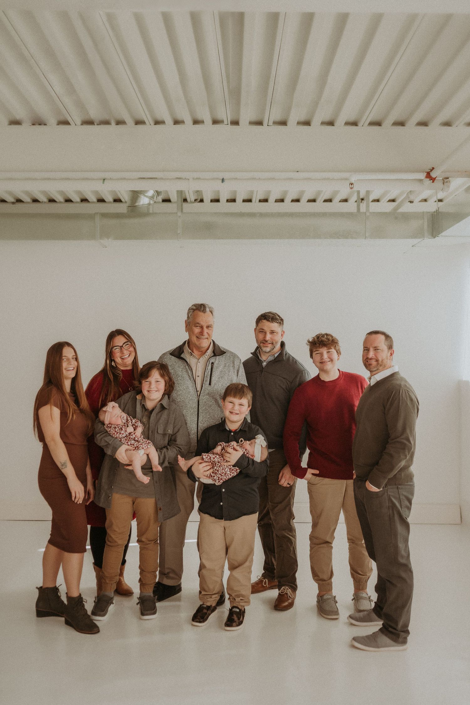 Extended family group poses together in coordinated casual attire in a bright white studio setting.