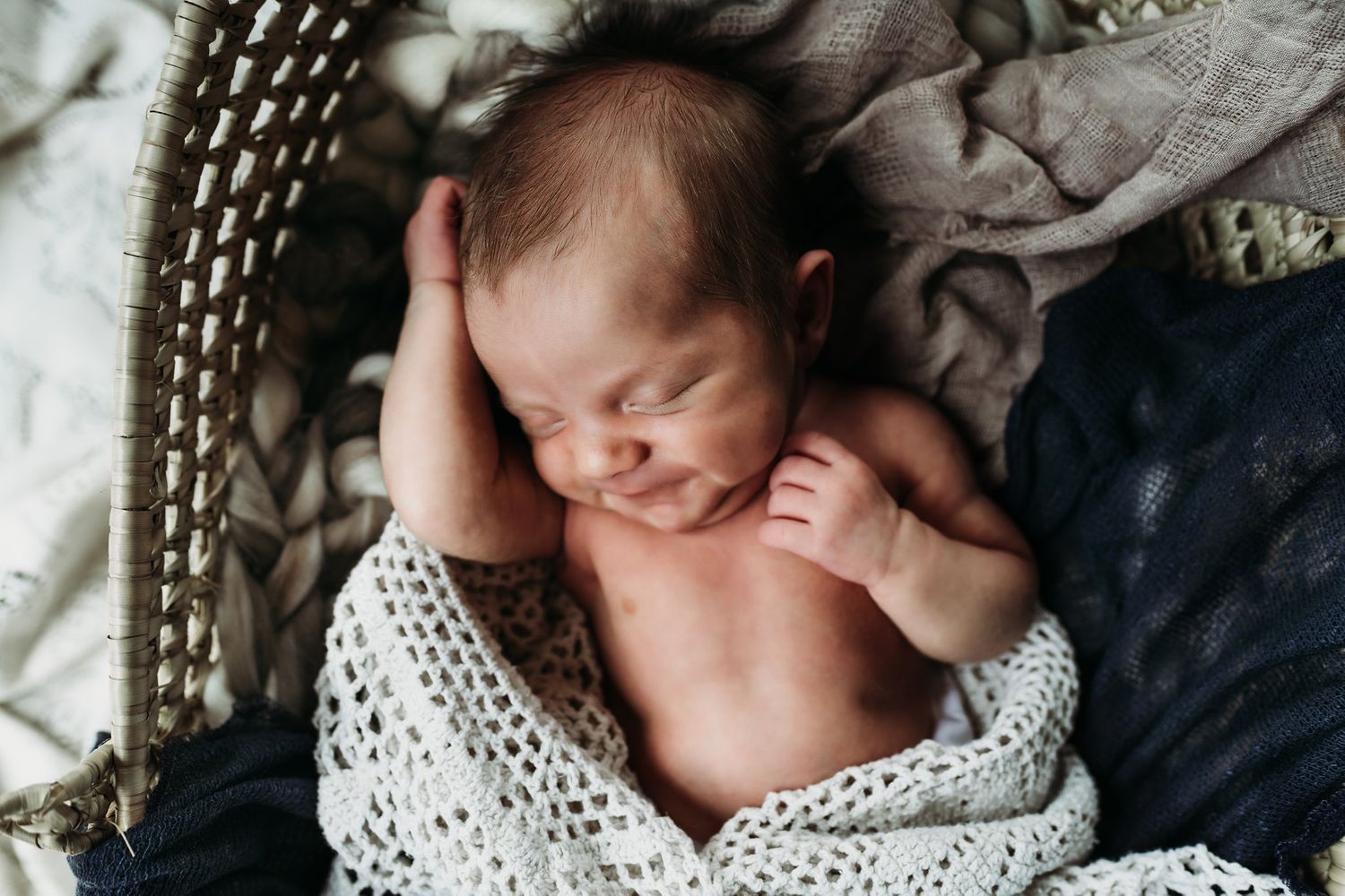Sleeping newborn peacefully resting in a woven bassinet with textured blankets.