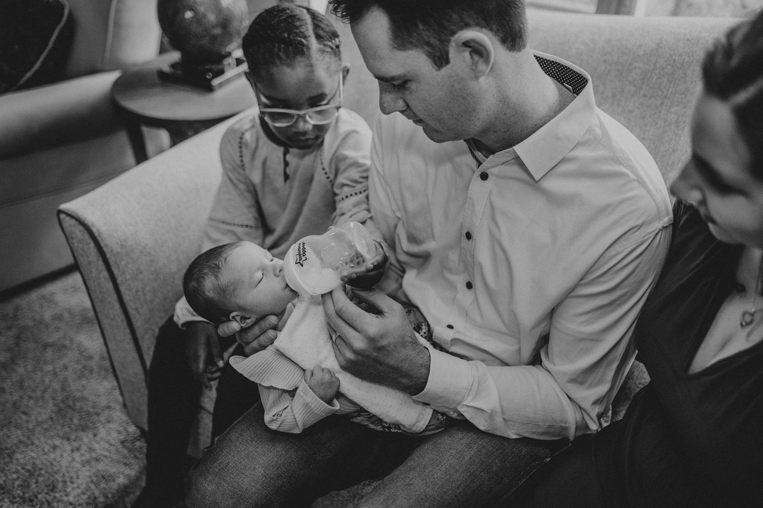 A black and white photograph showing caretakers gently holding and feeding an infant.