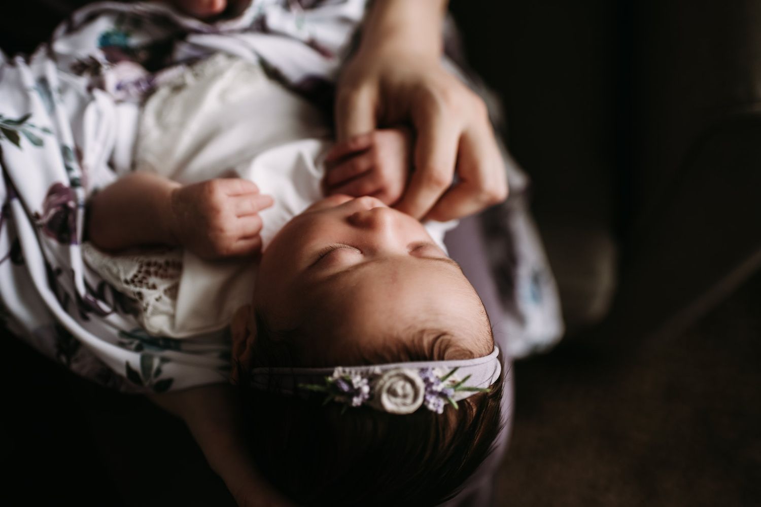 Overhead view of sleeping baby in floral outfit with hands tenderly touching their face.