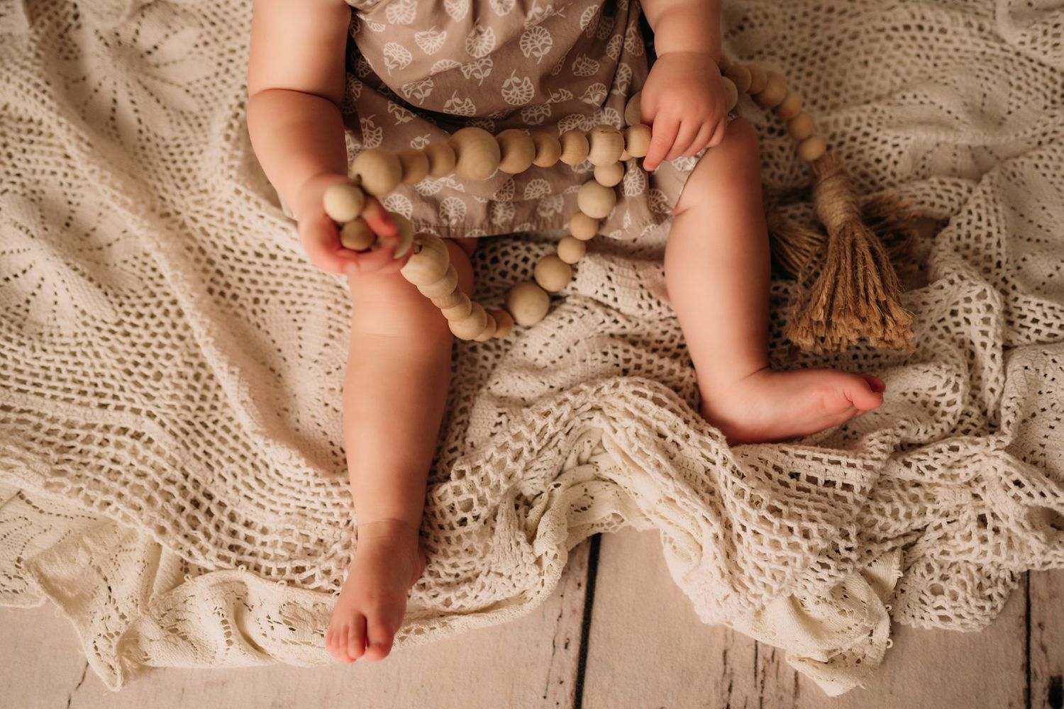 Close-up of small legs and wooden bead garland on cream lace blanket.