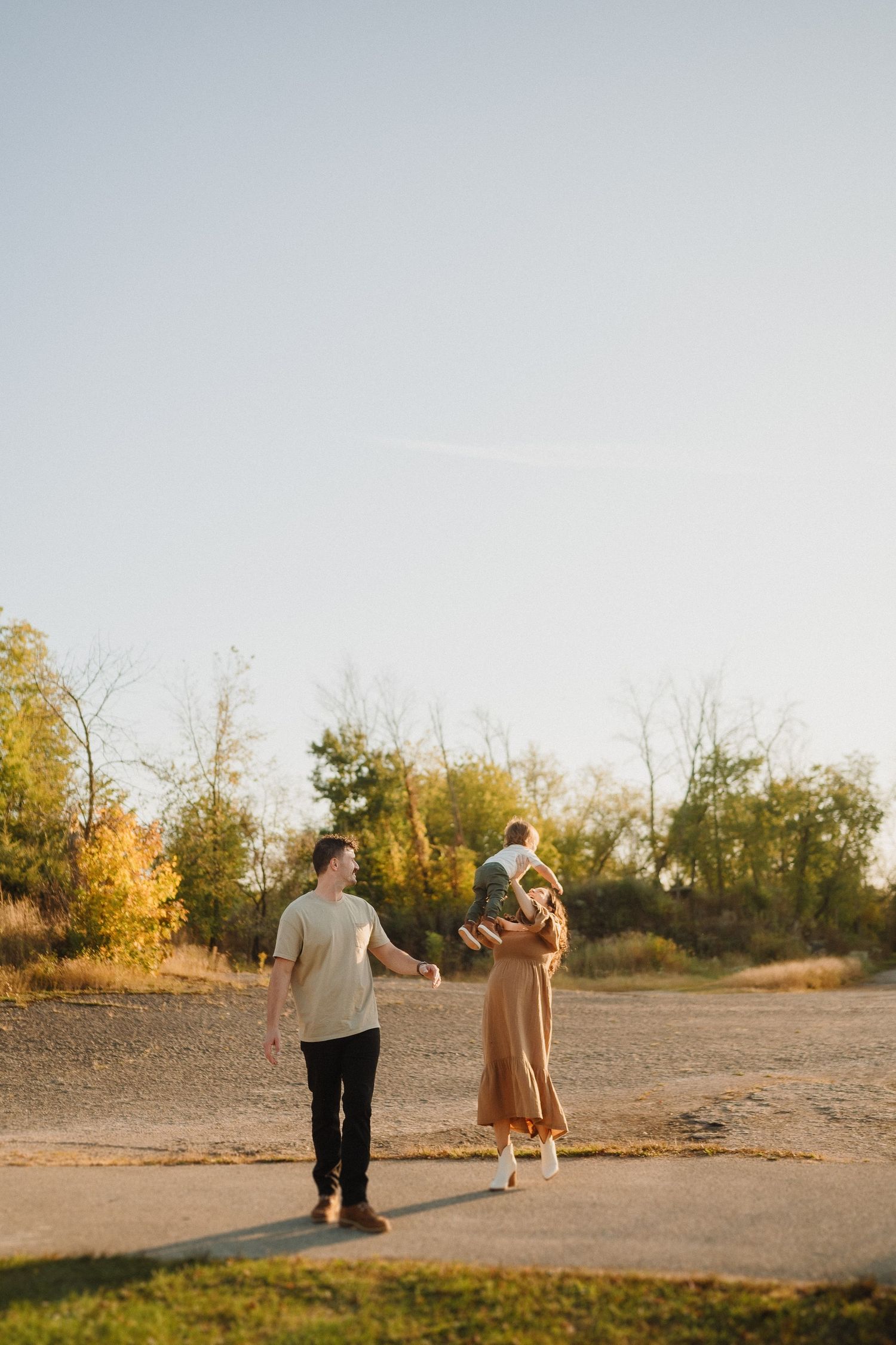 A couple walks together on a path during golden hour with autumn trees in the background.