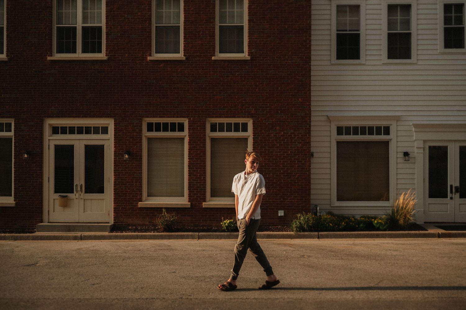 A person walks past brick row houses on a city sidewalk during a sunny day.