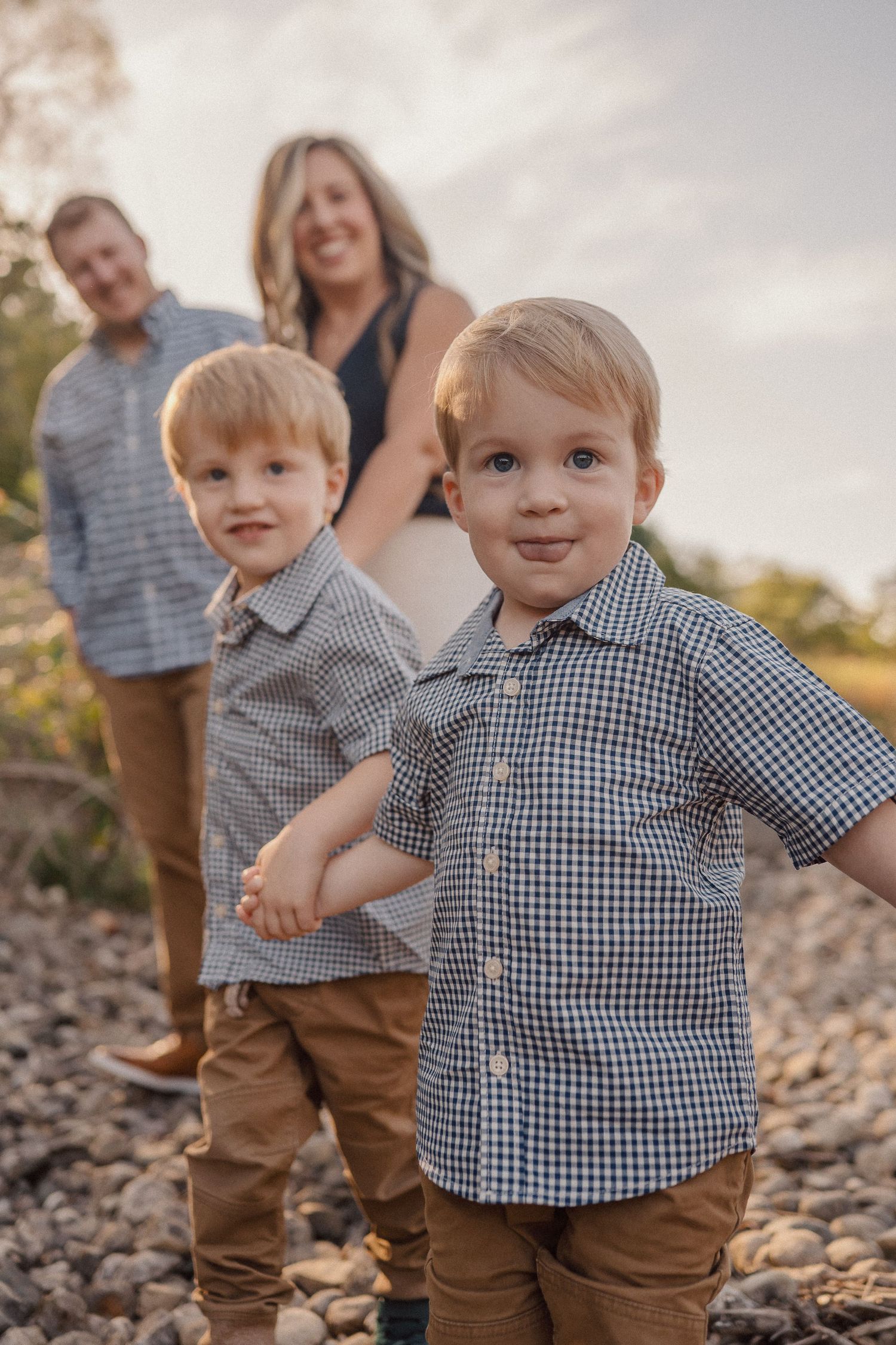Two young children in matching gingham shirts and khaki pants play on a rocky outdoor setting.
