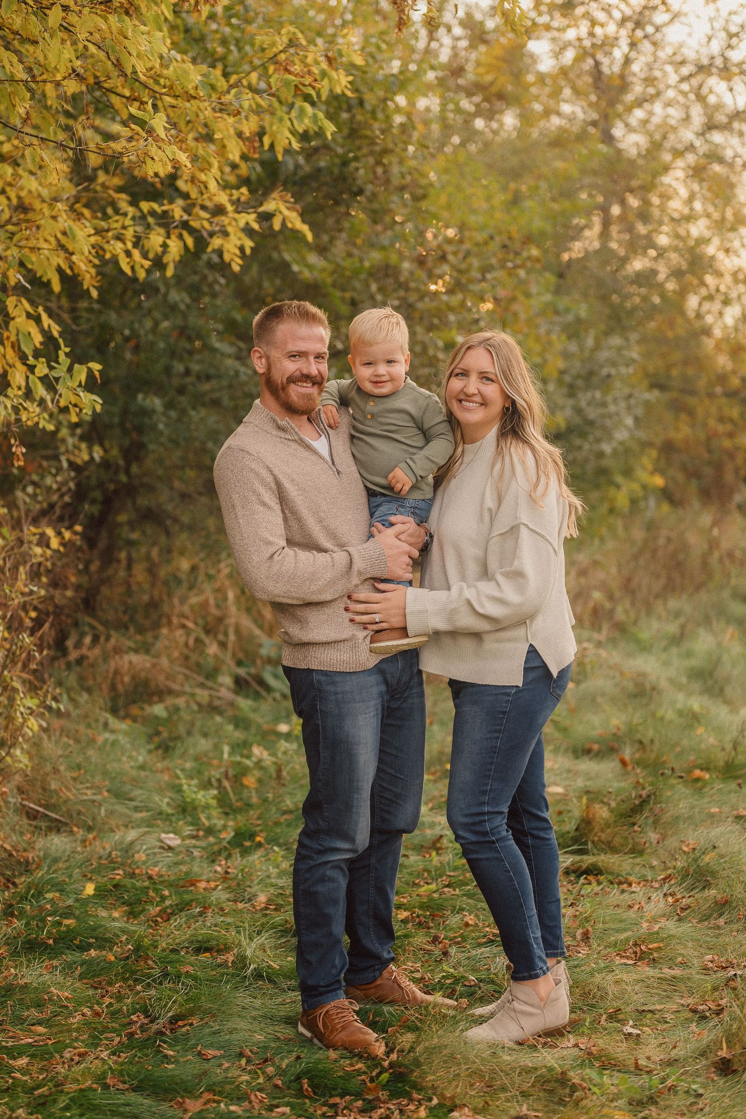 A family poses together outdoors in autumn with golden leaves and natural lighting.