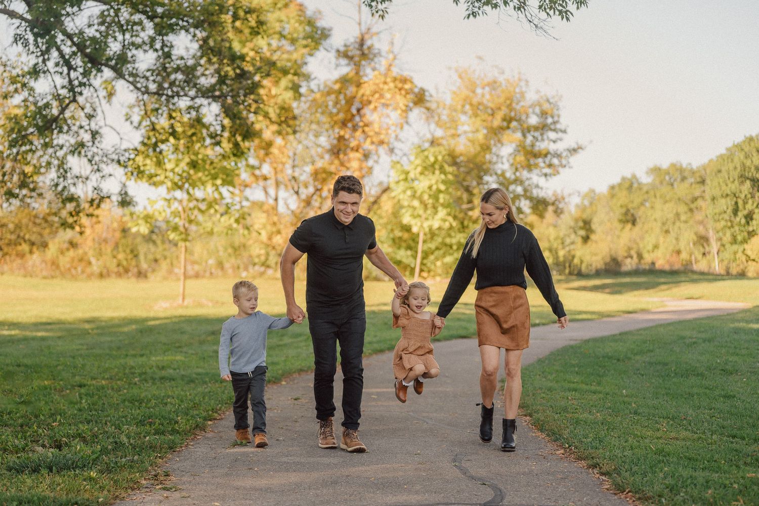 Family walking together on a path surrounded by autumn trees in warm sunlight.