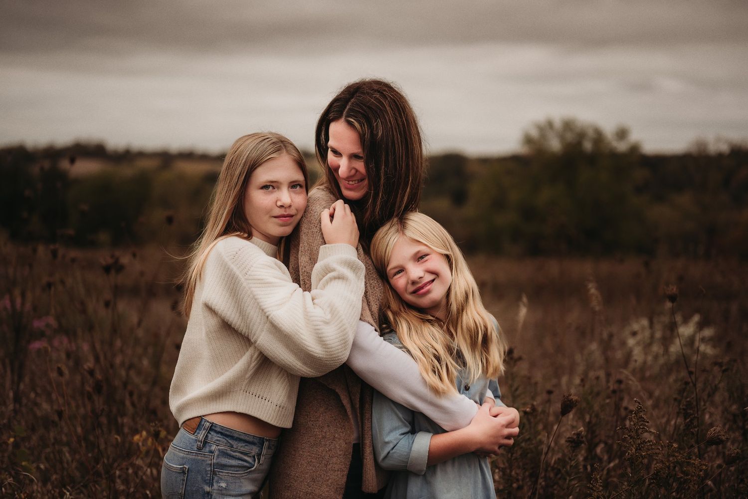 Three people share intimate moment while embracing in autumn field.