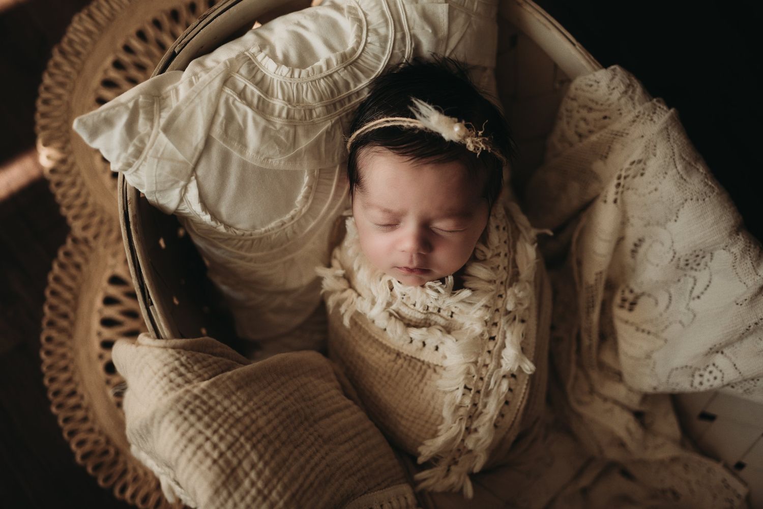Newborn baby sleeping peacefully in vintage wicker bassinet with cream bedding.