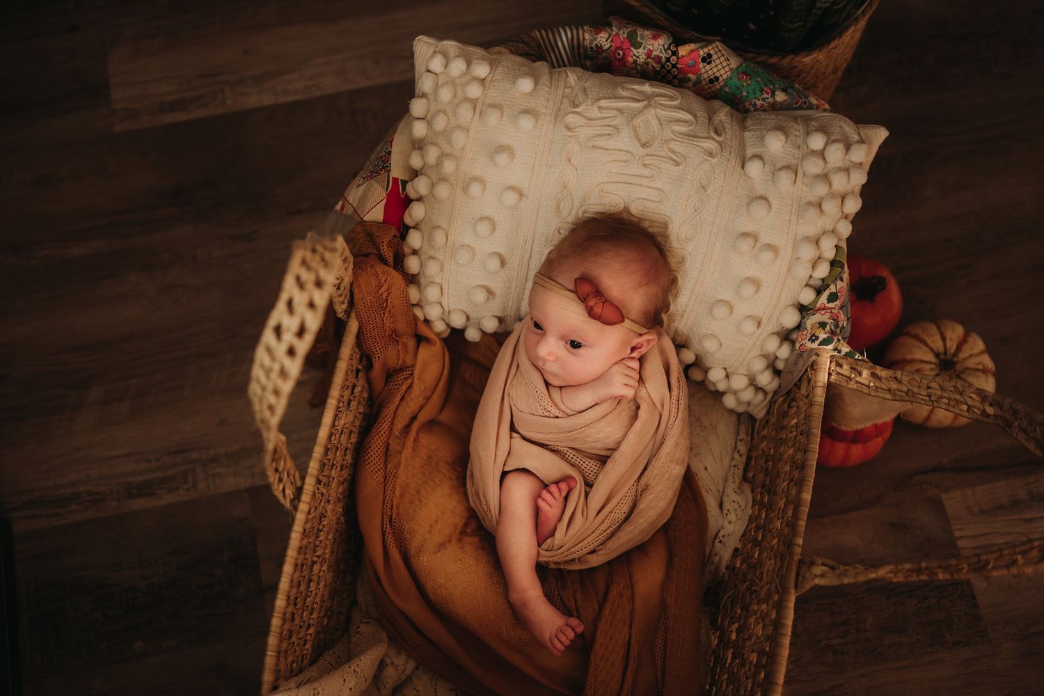 Newborn photography setup with pumpkins and autumn decorations on wooden floor.