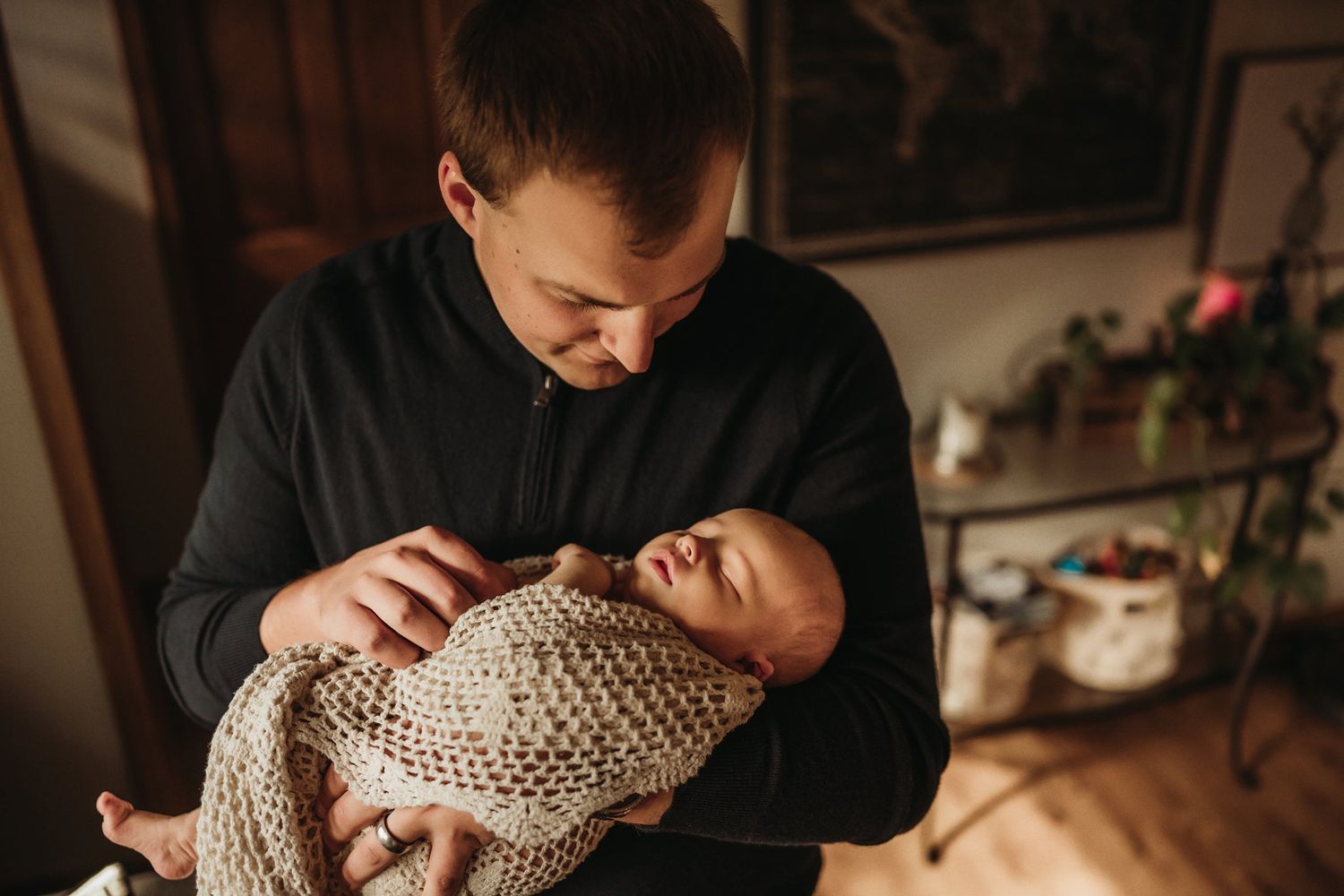 An intimate moment as someone in black cradles a baby wrapped in a knitted blanket.