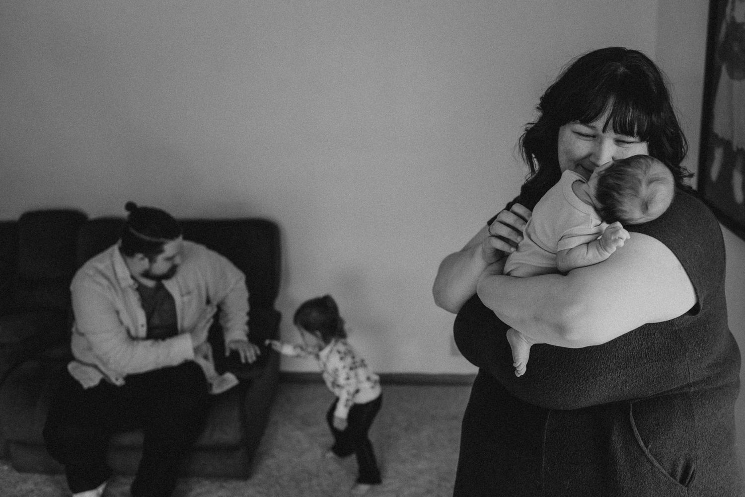 Black and white family scene with baby and adults in a living room.