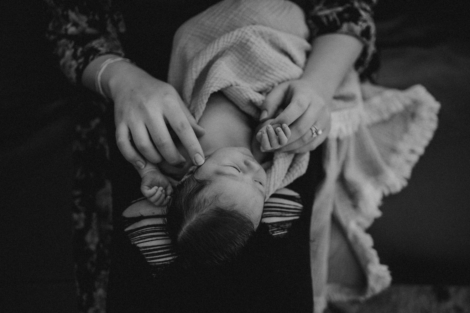 Intimate black and white photo of parent cradling newborn baby in gentle embrace.
