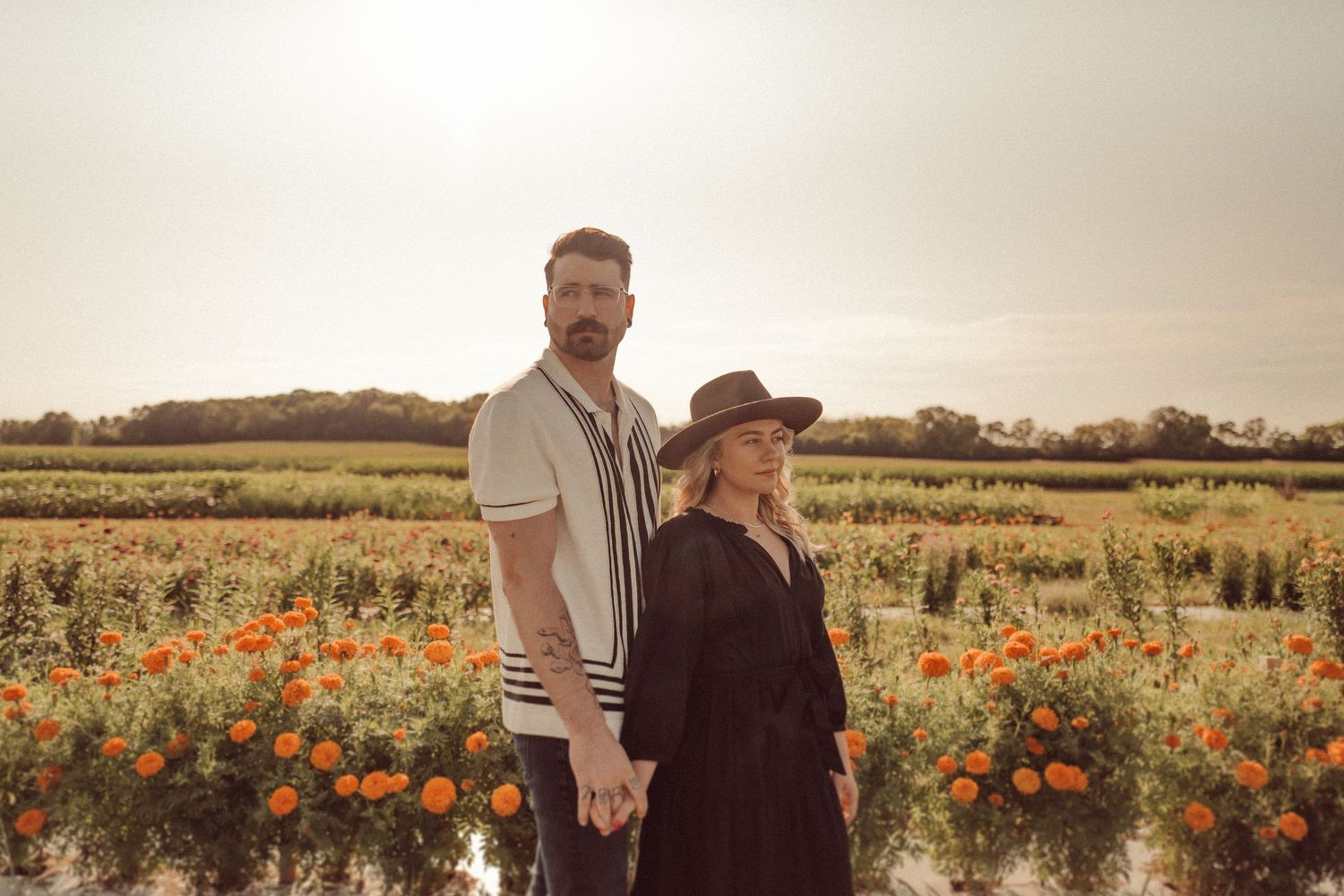 A couple stands together in a field of orange wildflowers during golden hour.