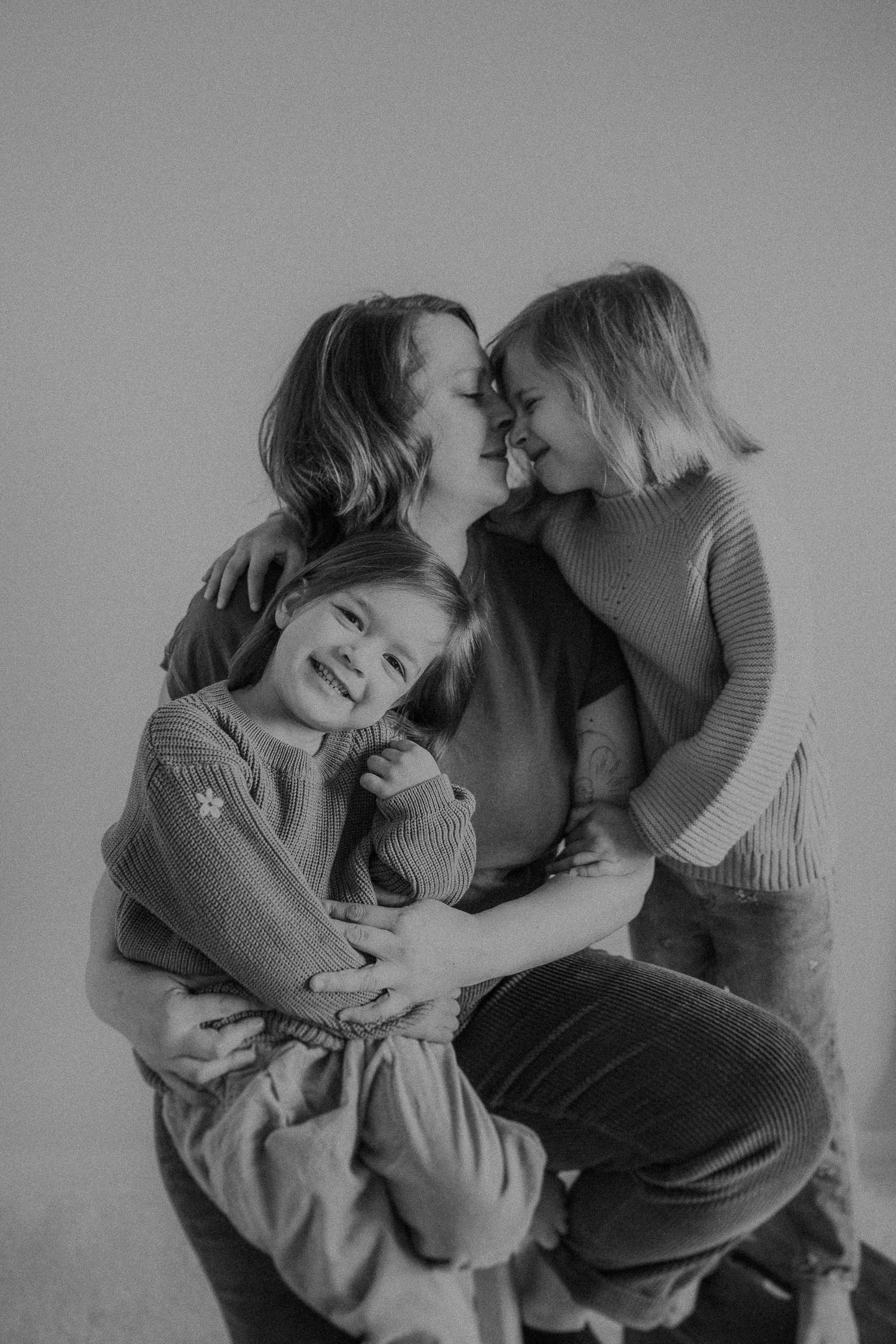 Black and white portrait showing tender embrace and laughter against neutral background.