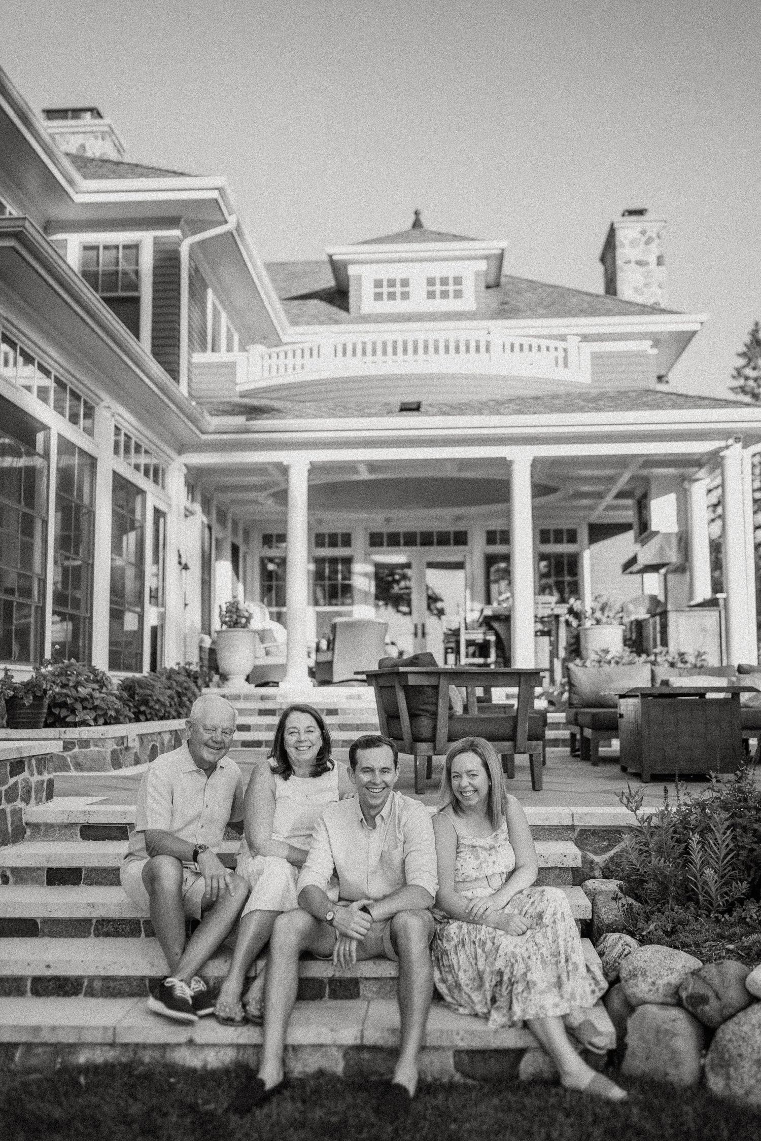 Family portrait on stone steps of a classic white colonial style home in black and white.