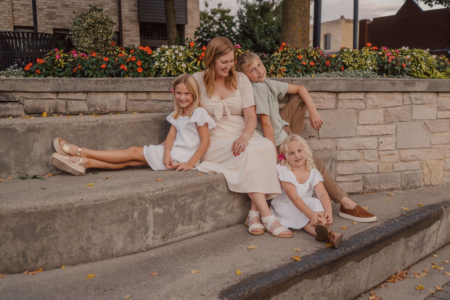Family members relaxing together on a stone wall near colorful flowers.