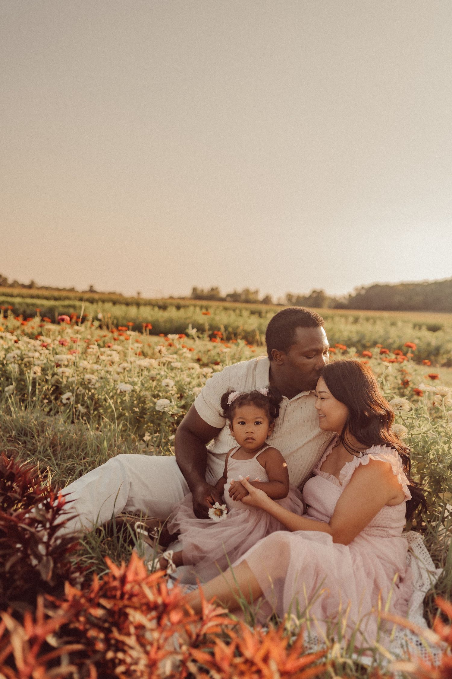 A loving family moment captured in a field with orange flowers at sunset.