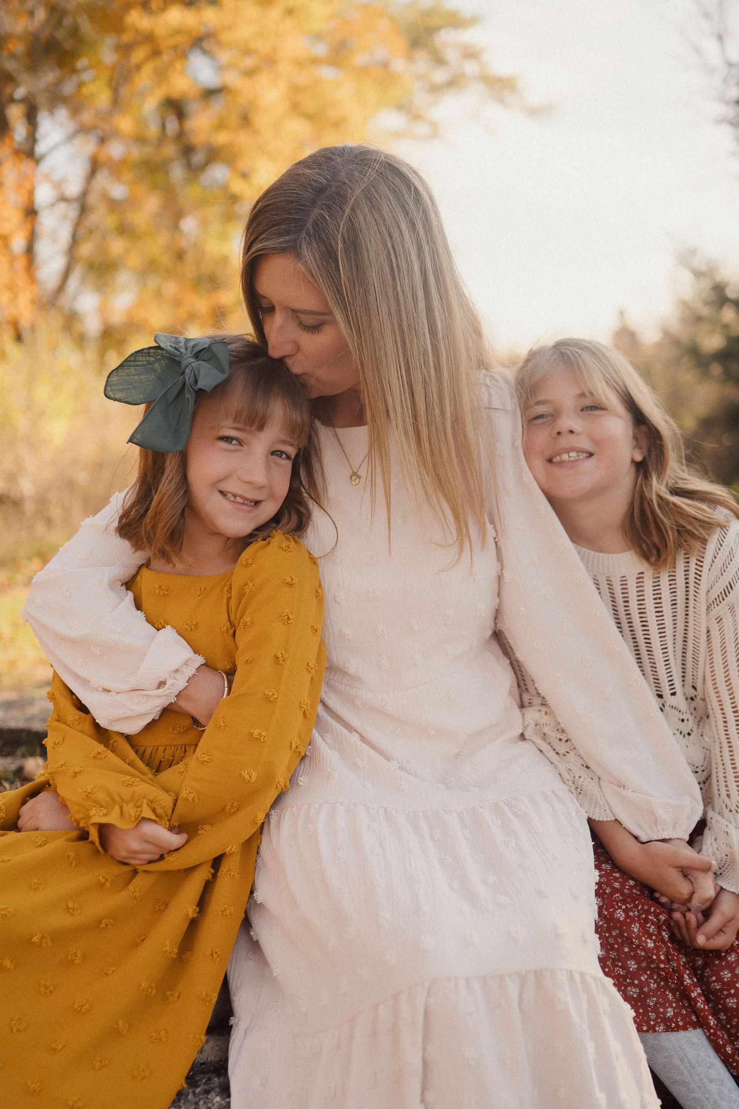 Family shares tender moments together during autumn photoshoot with golden leaves and warm colors in background.