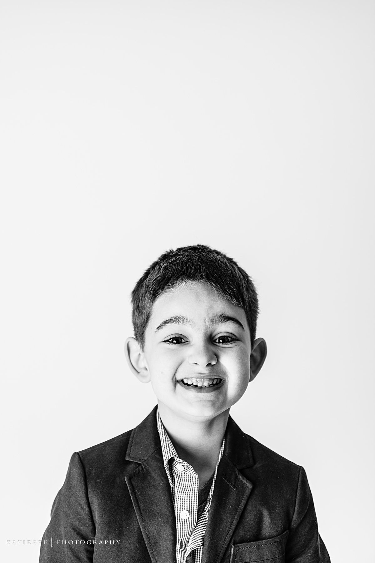 Black and white studio portrait of smiling child wearing dark blazer and striped shirt.
