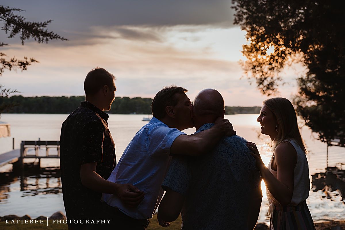 Silhouetted figures embracing during a lakeside sunset gathering.