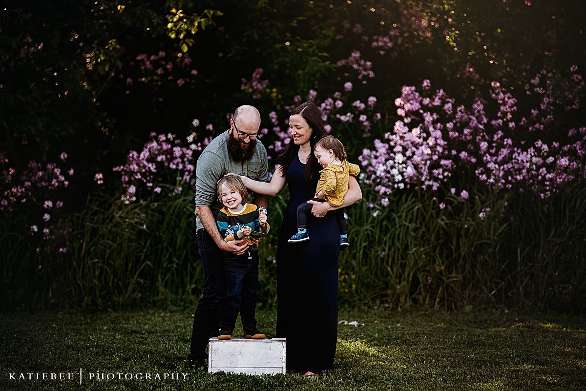 Family portrait at dusk with purple wildflowers creating a magical garden setting.
