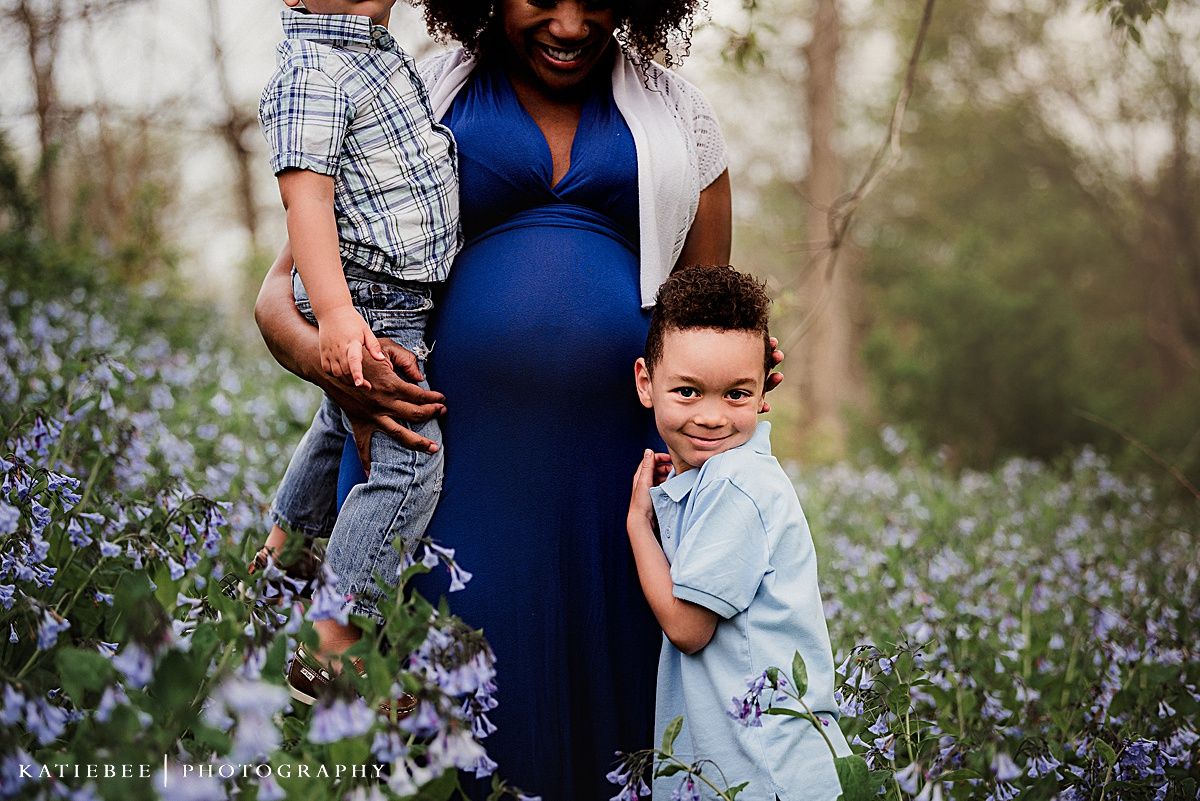 Maternity portrait with children in blue dress among purple wildflowers.