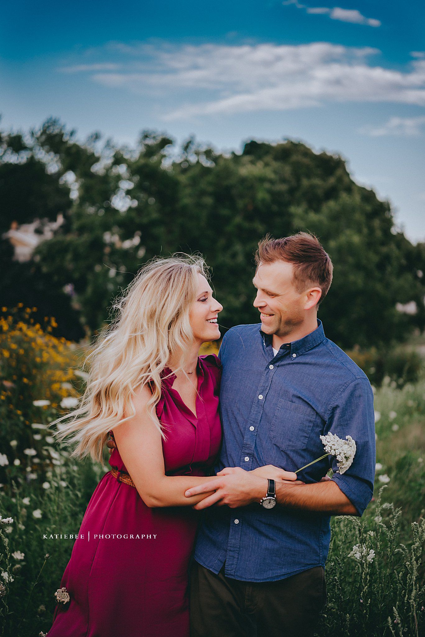 Couple sharing a joyful moment in a field of yellow wildflowers against blue sky.