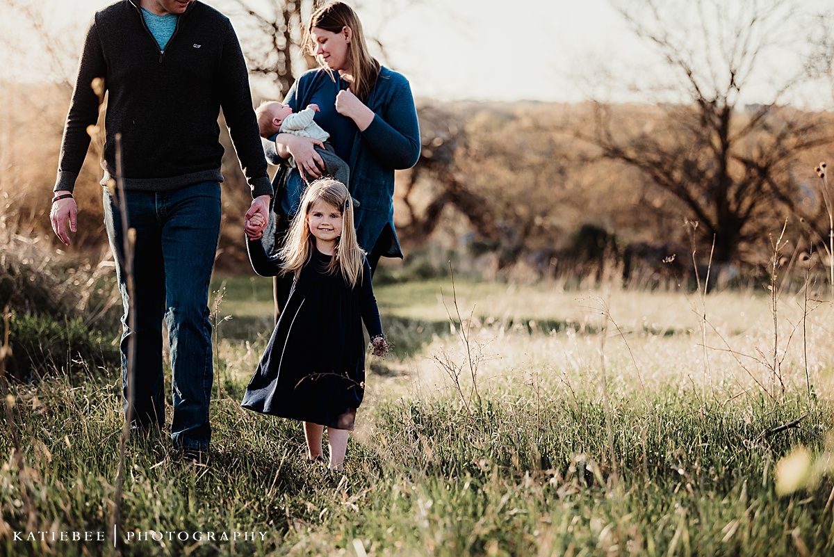 Family walking together through tall grass in golden evening light.