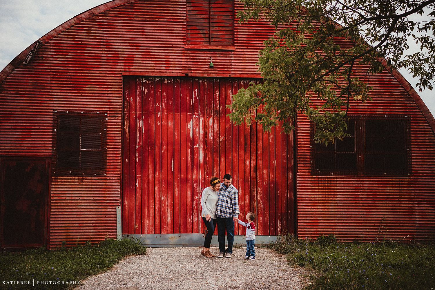 A small group stands in front of a large red barn with rustic sliding doors.