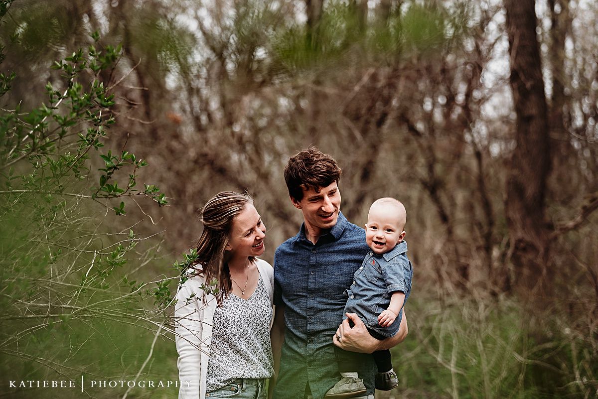 Natural outdoor family portrait in wooded setting with green foliage.