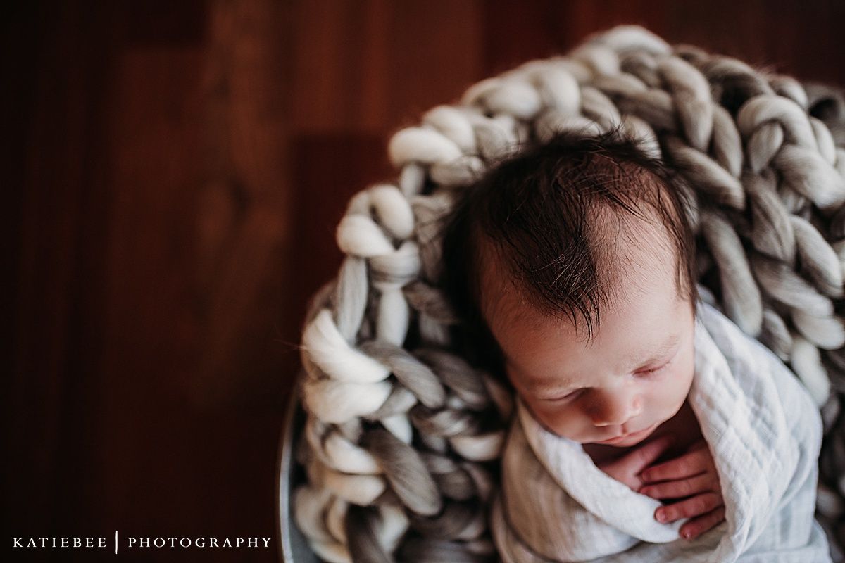 Newborn baby wrapped in chunky knit blanket during lifestyle photo session.
