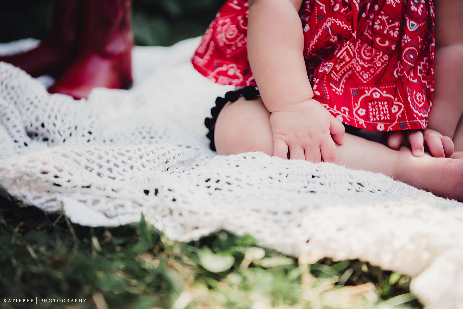 Small feet and red dress detail on white lace blanket outdoors.