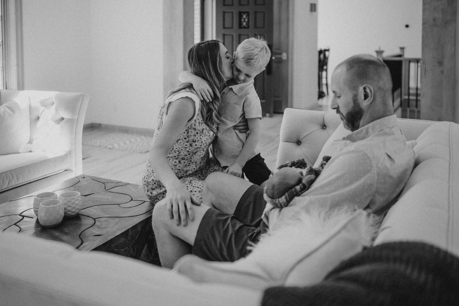Black and white candid photo of tender family moment on living room couch.