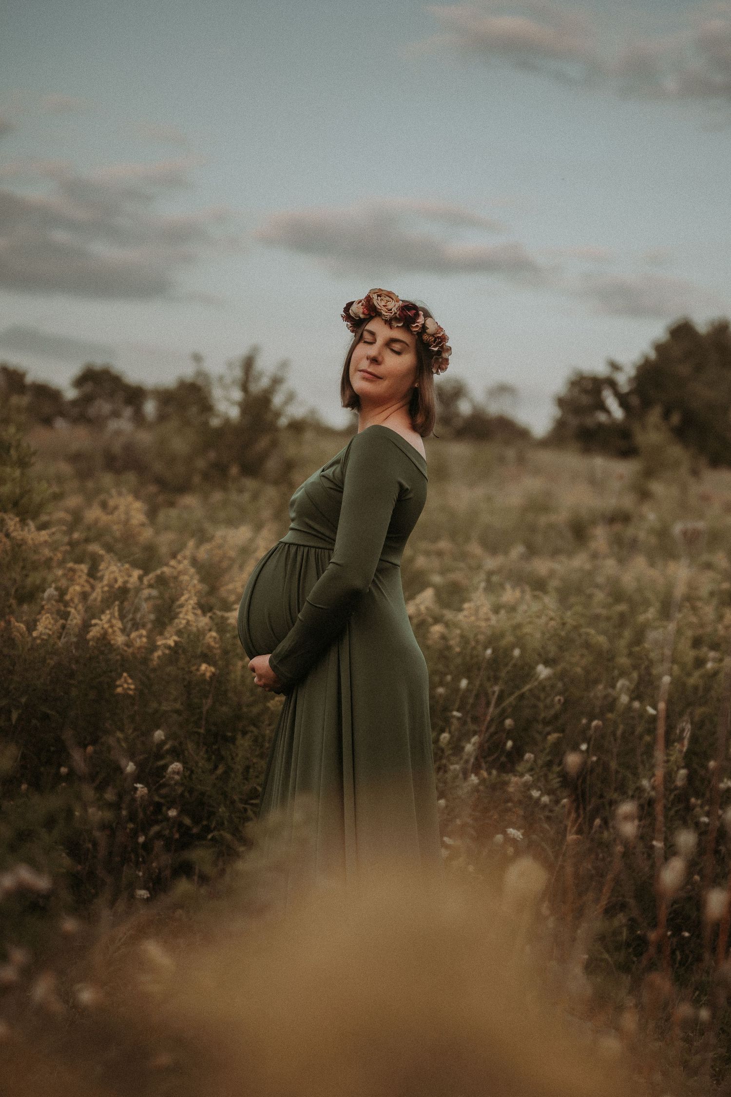 A maternity photo shows an expectant mother in a green dress amid tall grasses at sunset.