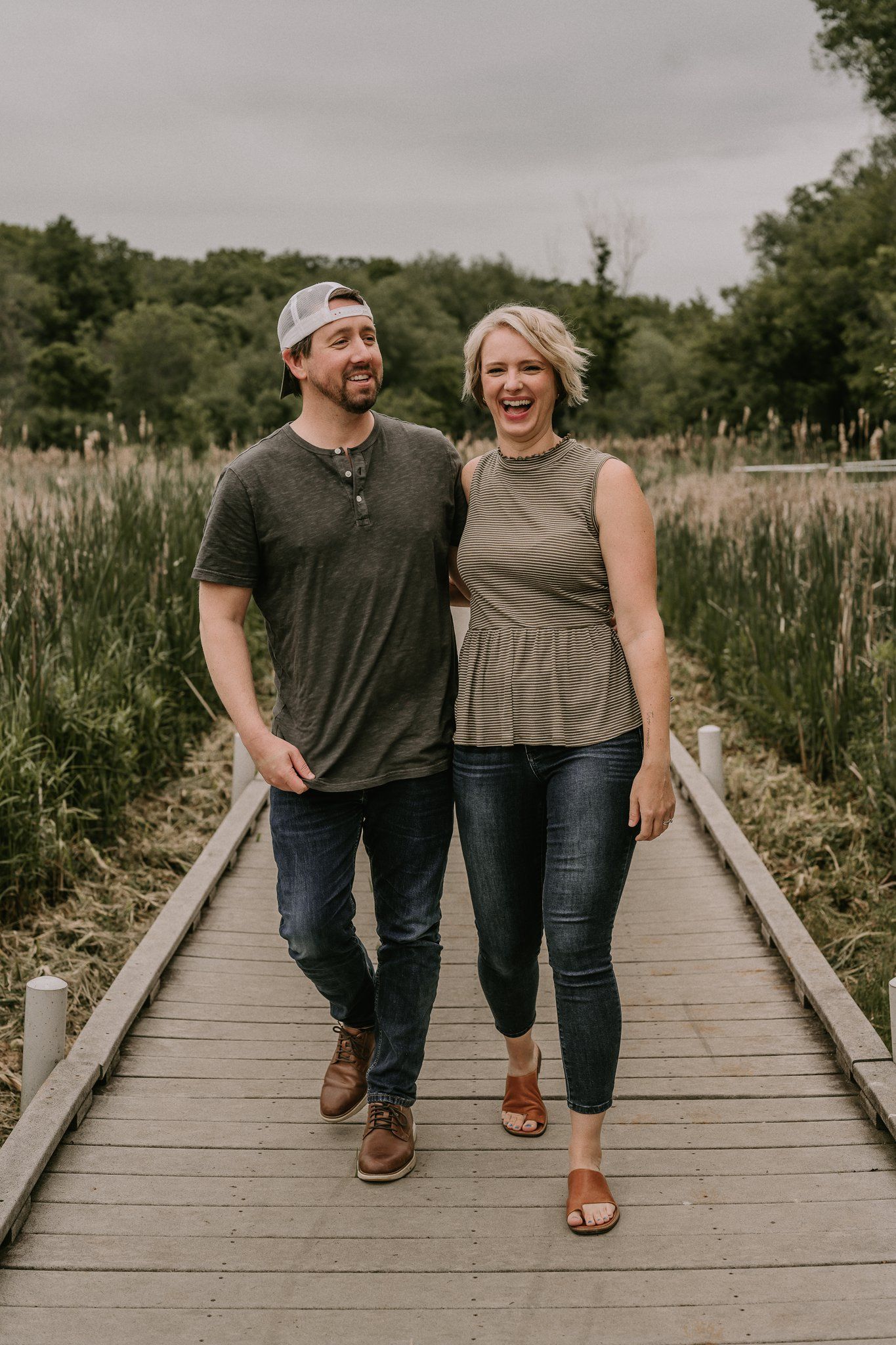 Couple sharing a laugh while walking on a wooden path through tall grass.