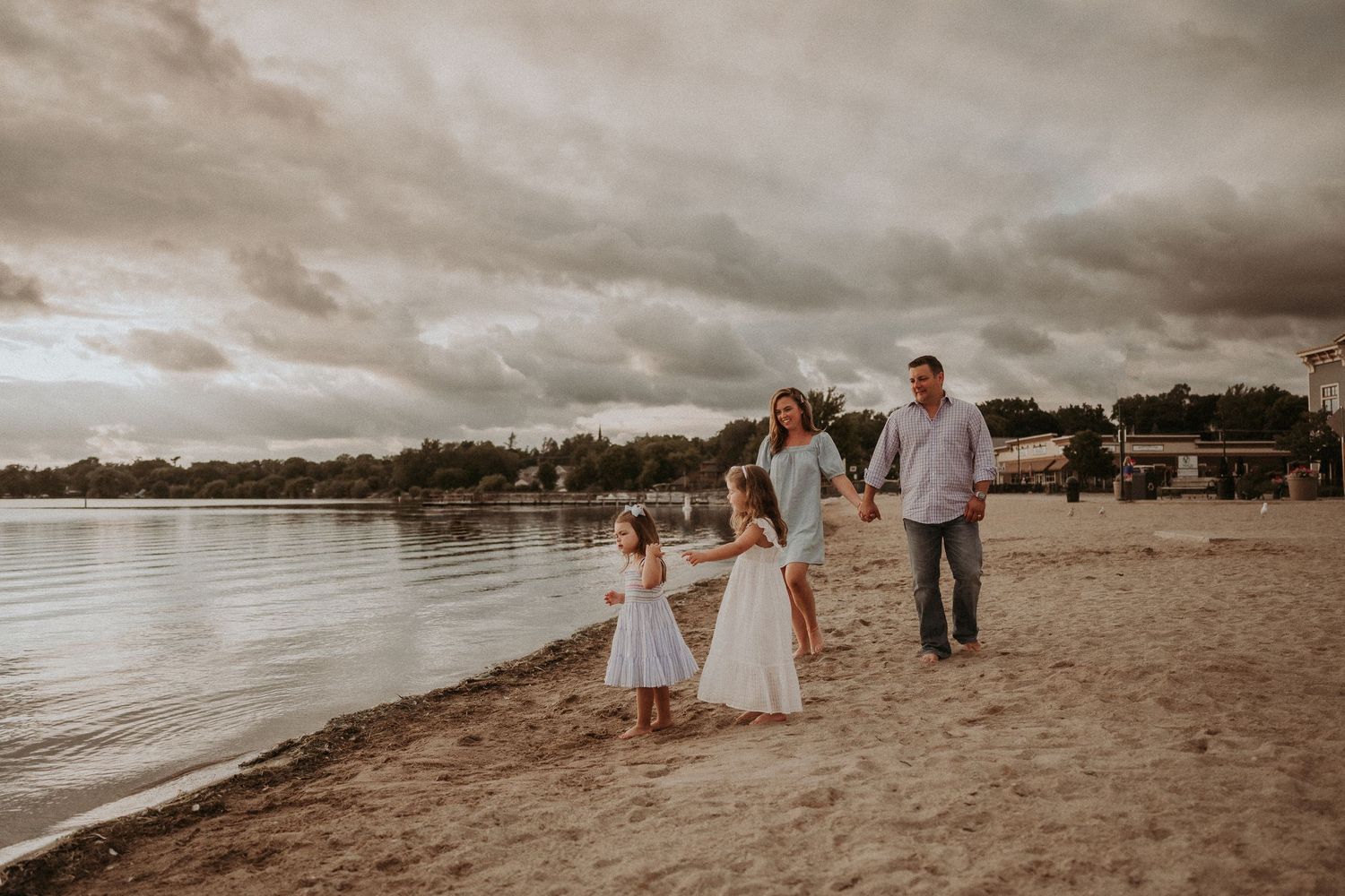 Family walking together on sandy beach with moody cloudy sky overhead.