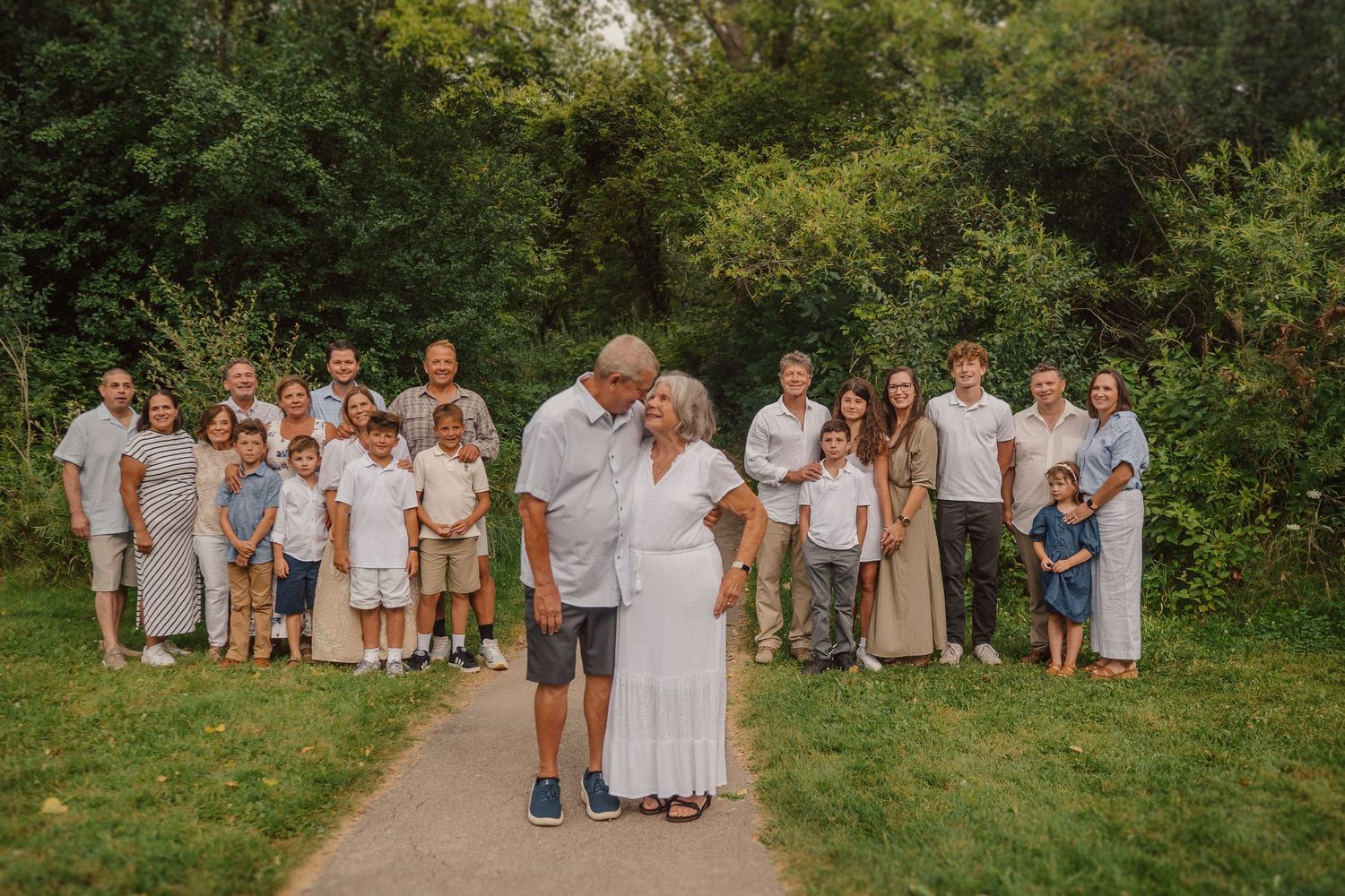 A large gathering of people in light-colored clothing pose for a group photo on an outdoor pathway.