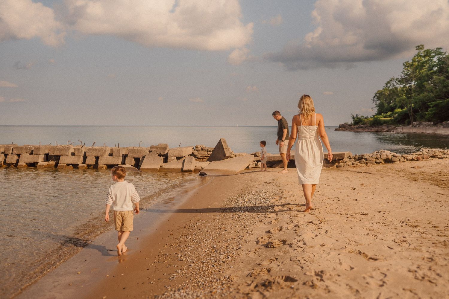 Two people walking along a beach shore with a wooden jetty in the background during golden hour.