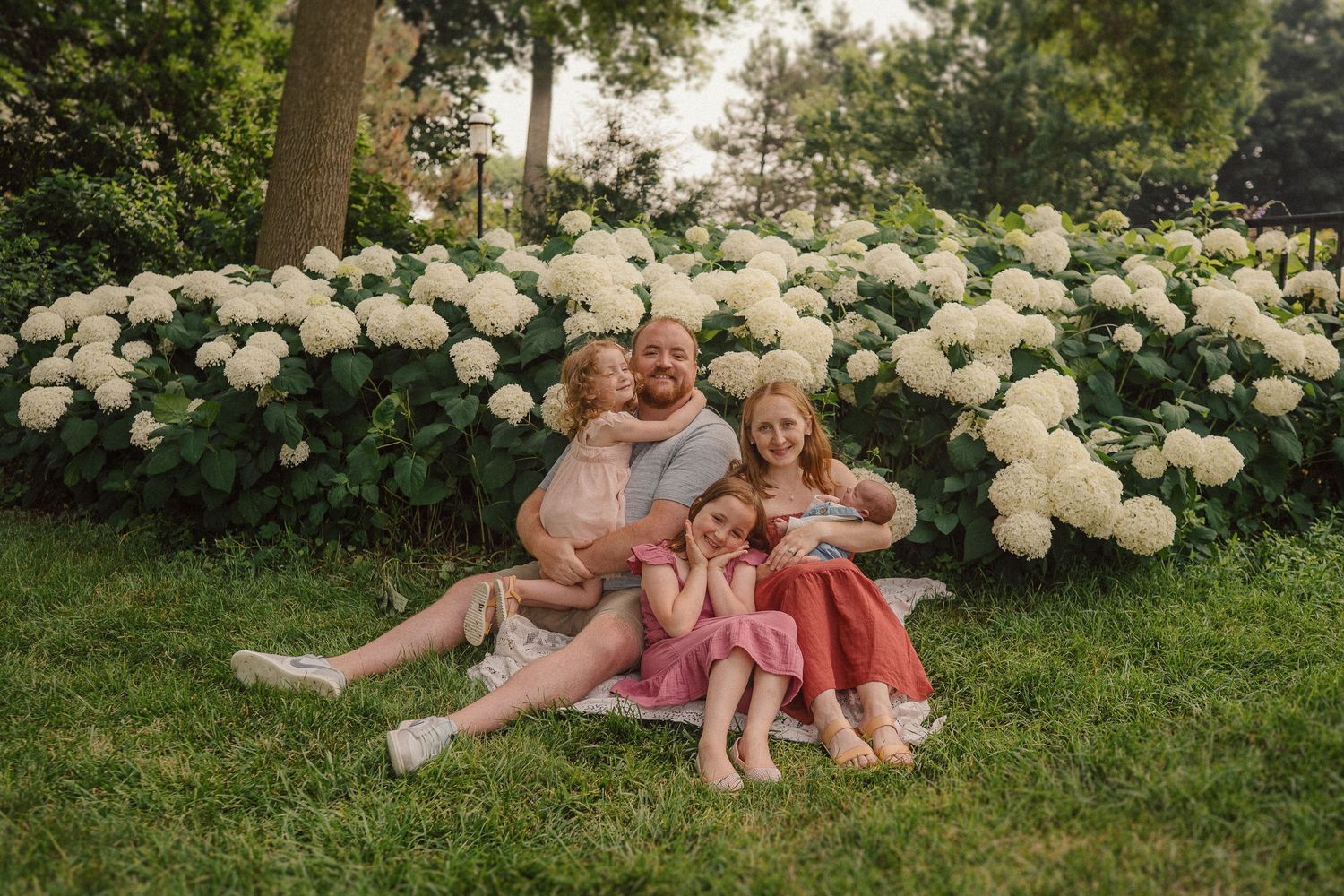 Family enjoying a relaxed moment together on grass surrounded by blooming white hydrangeas.