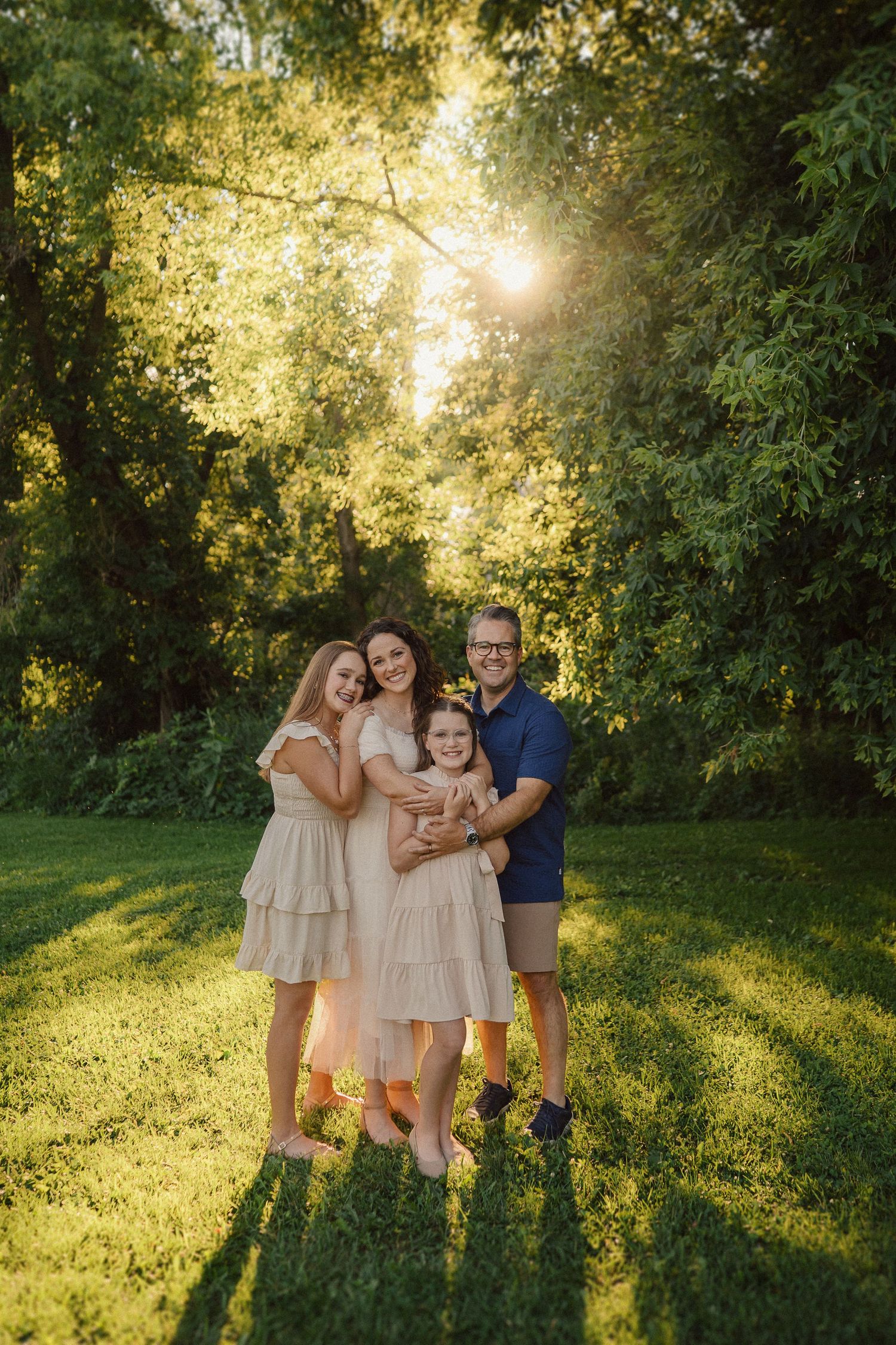 A family poses together in a sunlit garden setting with golden light streaming through trees.