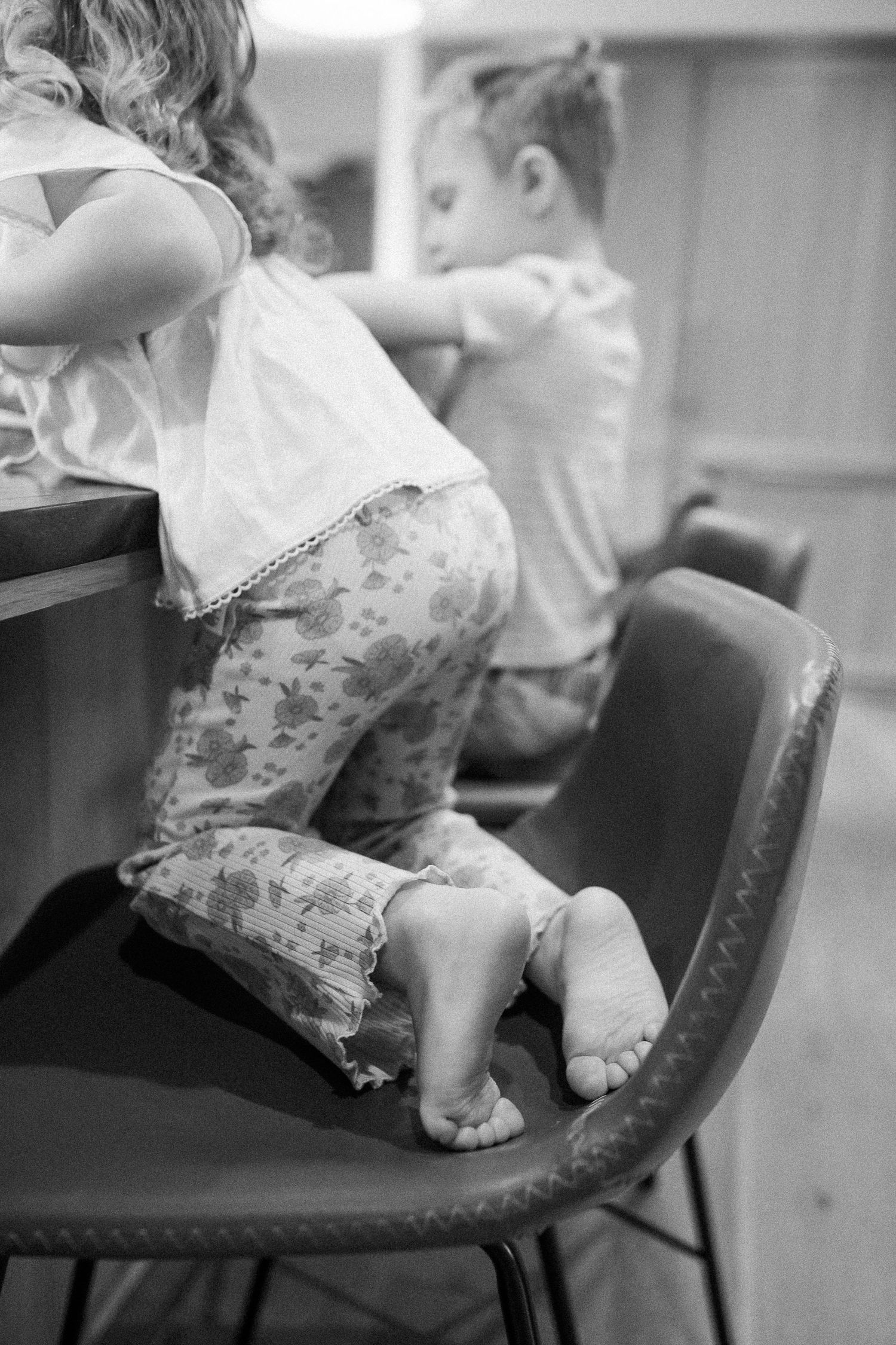 Two young children sitting on chairs at kitchen counter, black and white photo.