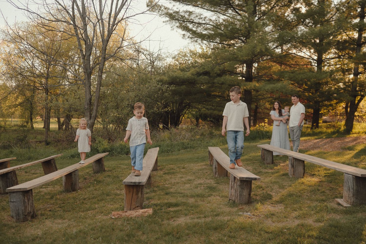 Family with children balancing on rustic wooden benches in a park during golden hour.