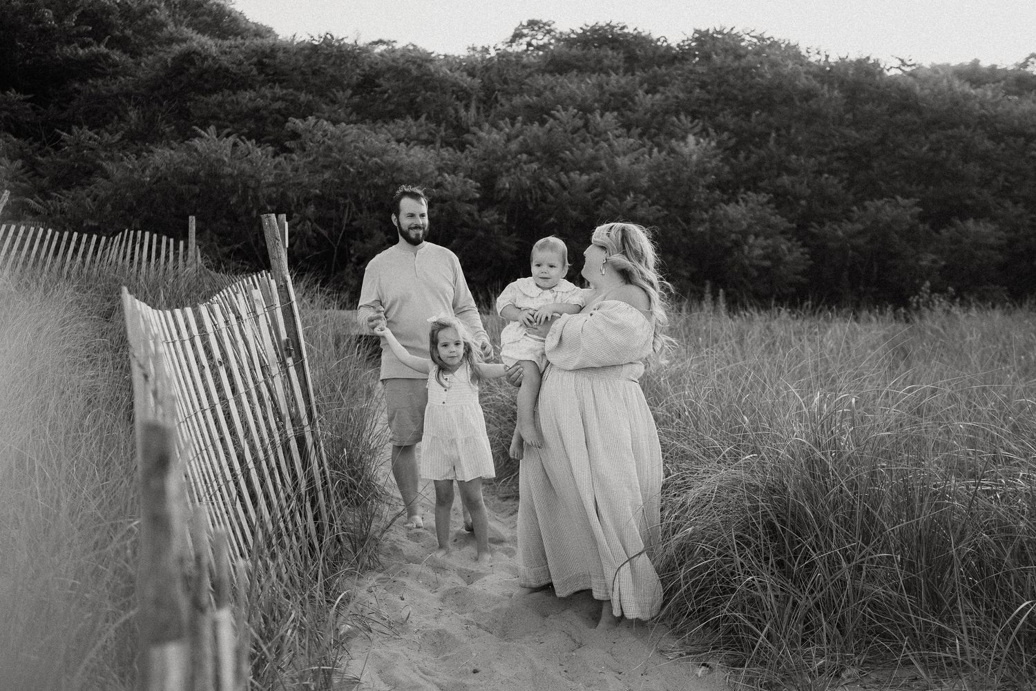 Black and white family portrait on sandy beach path with dunes.
