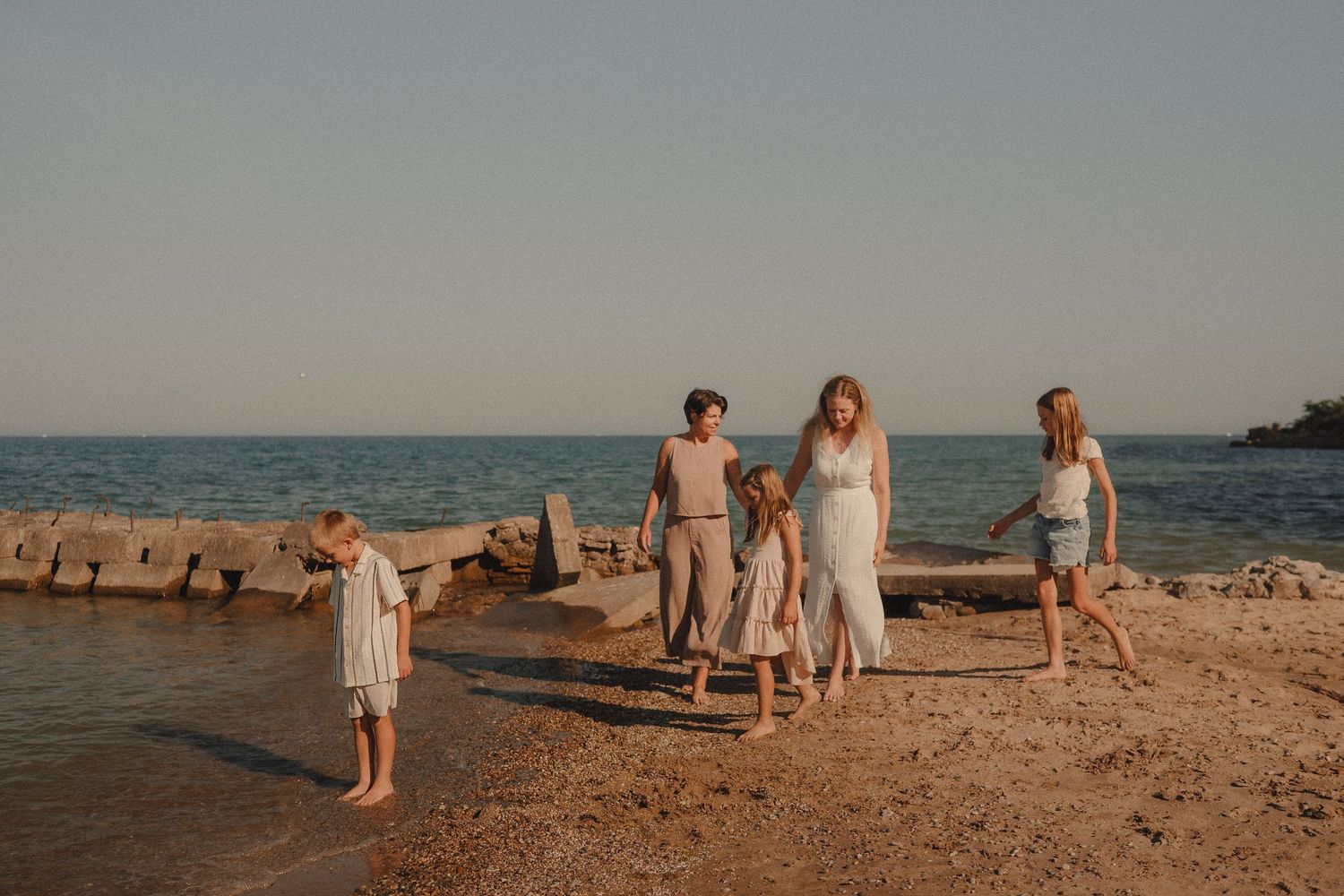 A woman and four children walk along a rocky beach shoreline during golden hour sunset light.