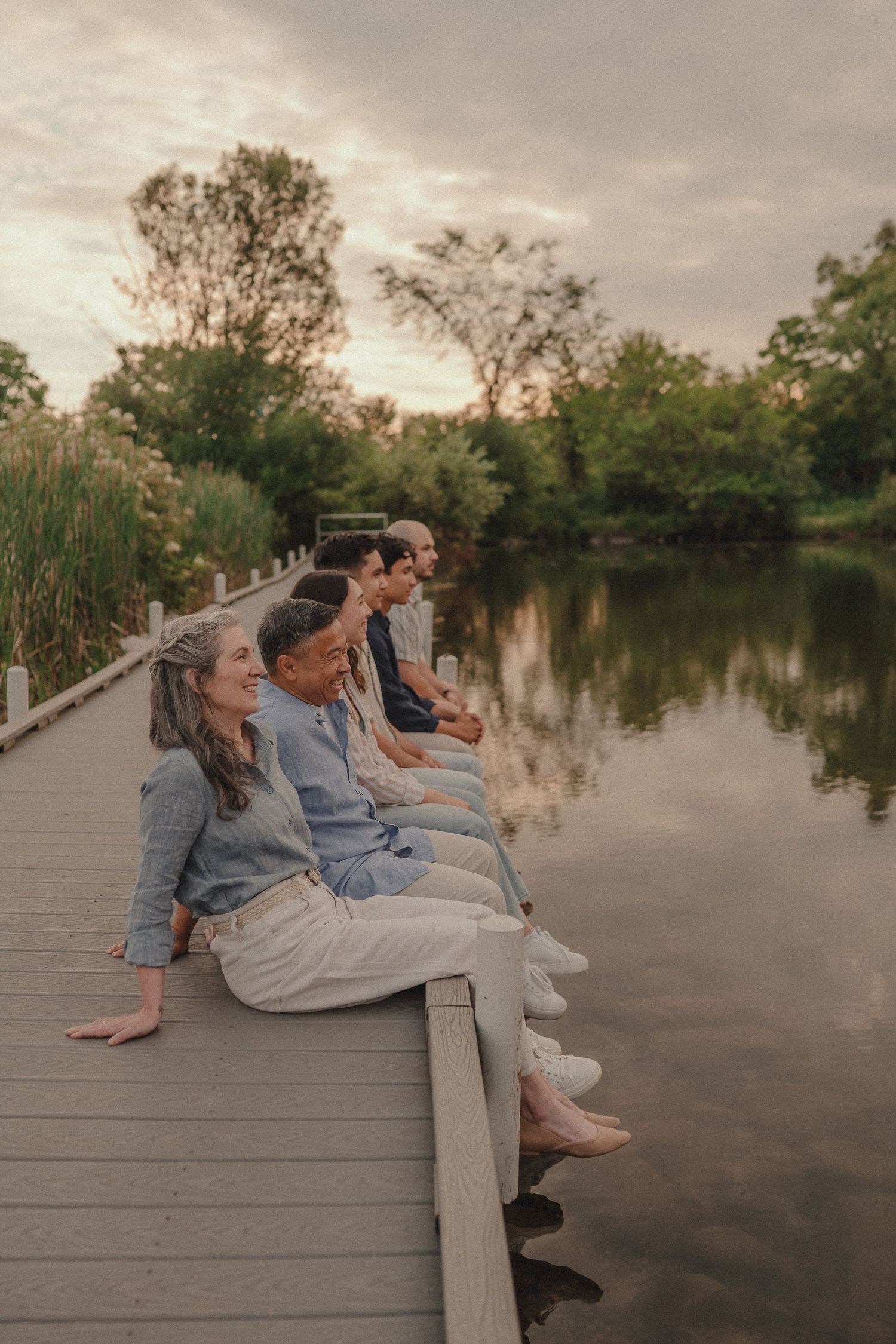 Family group sitting on a wooden dock by a calm reflective lake at sunset.