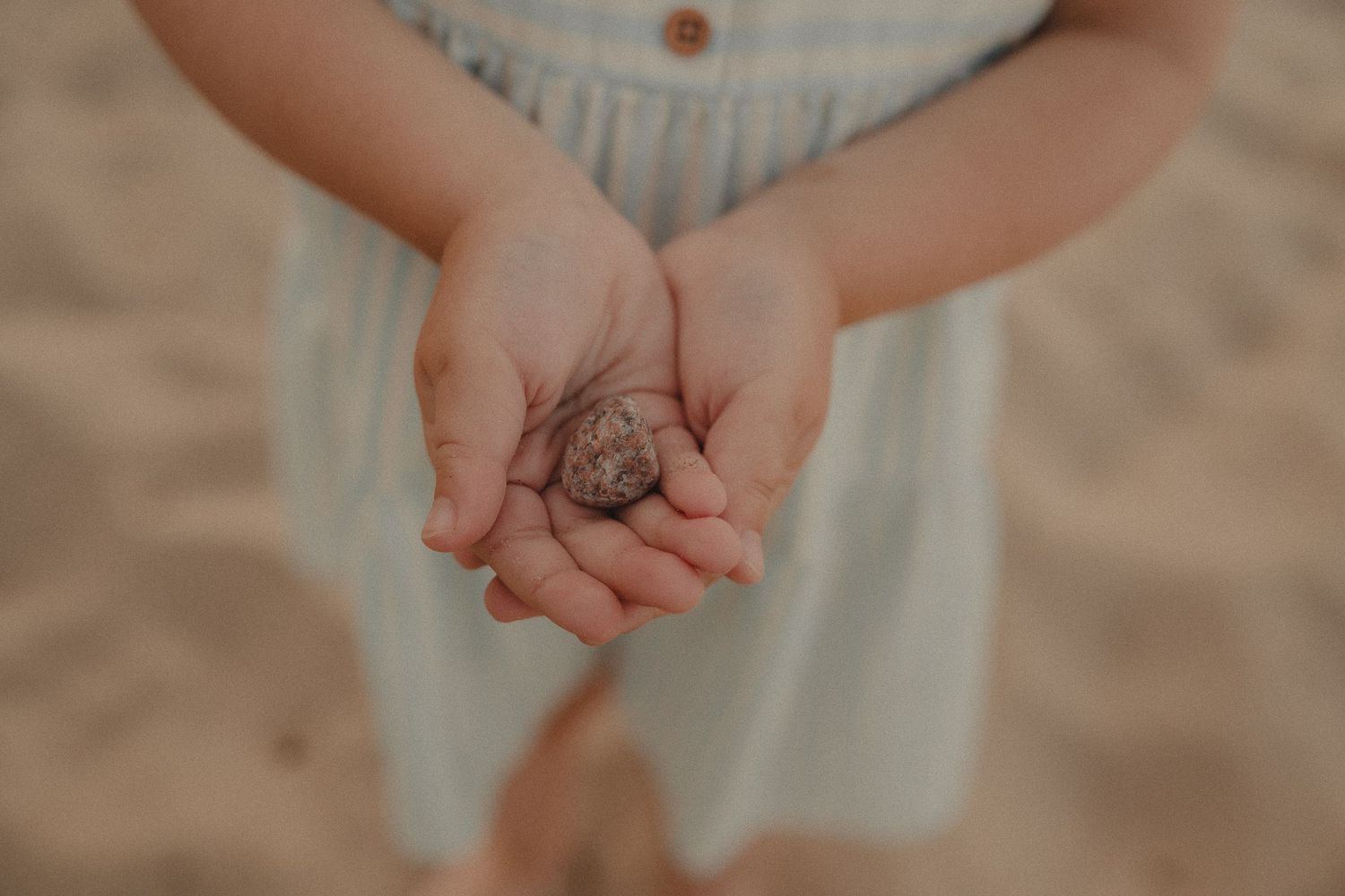Close-up of child holding a small shell in cupped hands on beach.