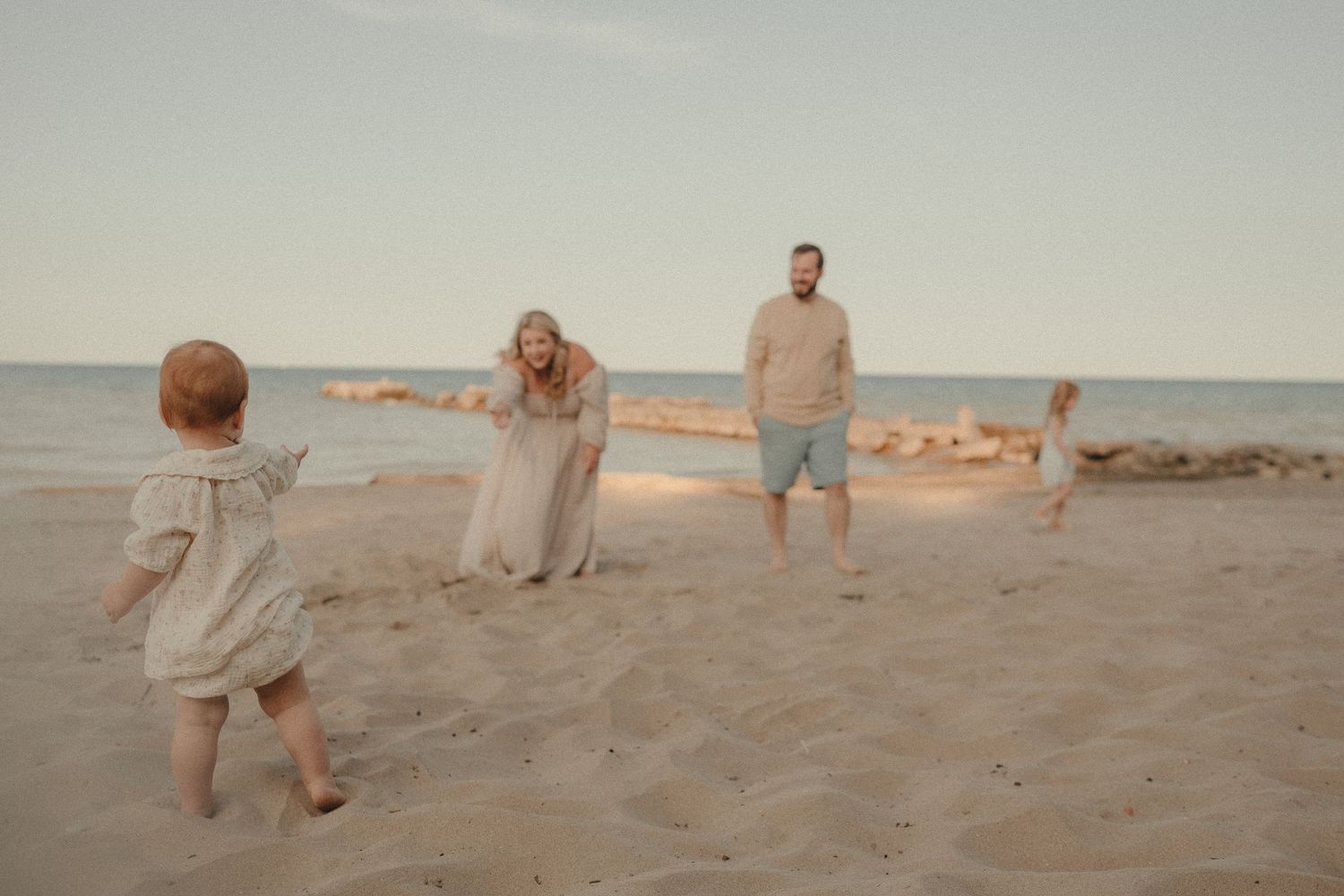 Family playing on a sandy beach at sunset, with parents and young children enjoying a casual outdoor moment by the sea.