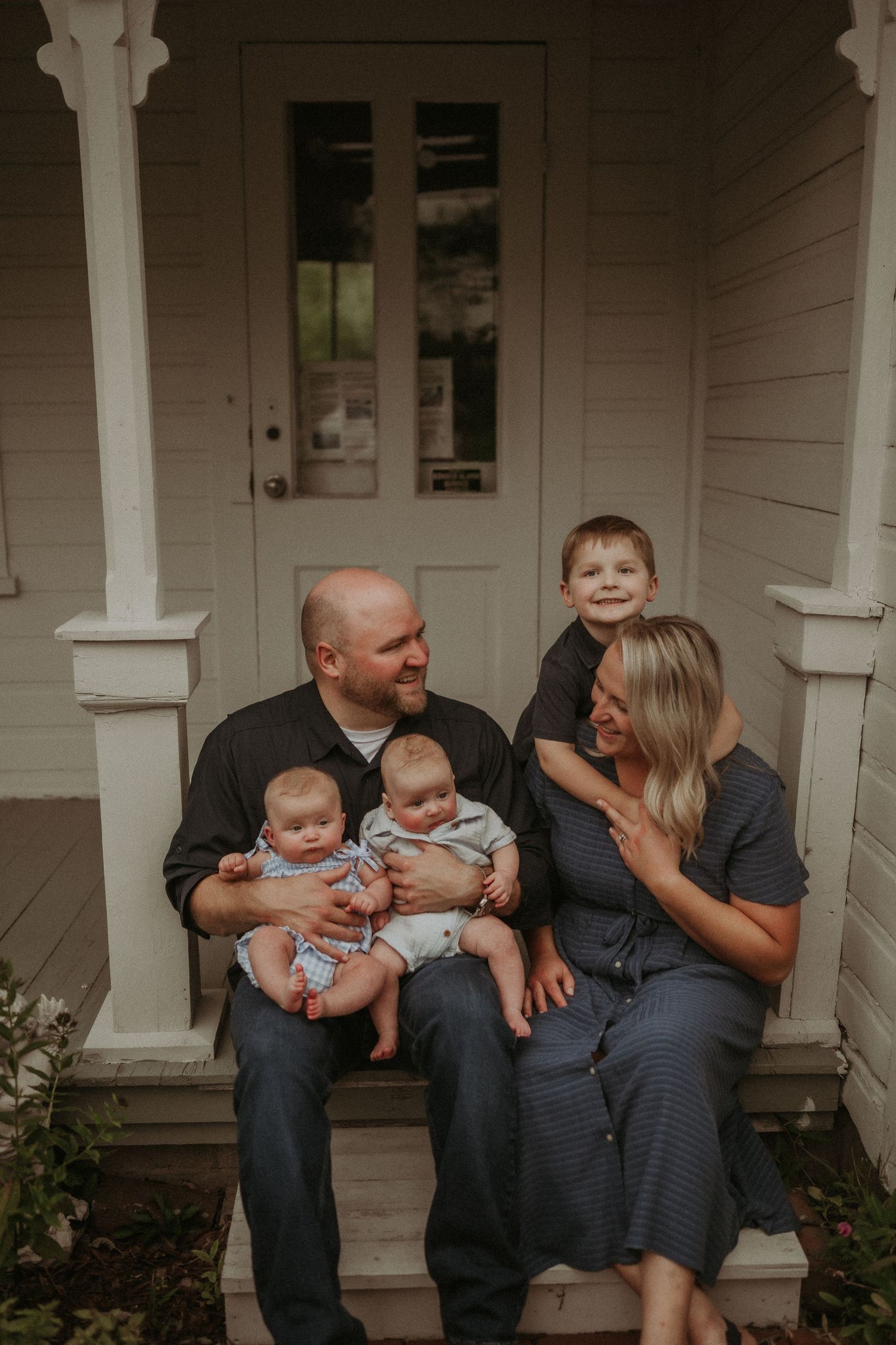 Family gathered on a vintage porch with white pillars share joyful moment together.