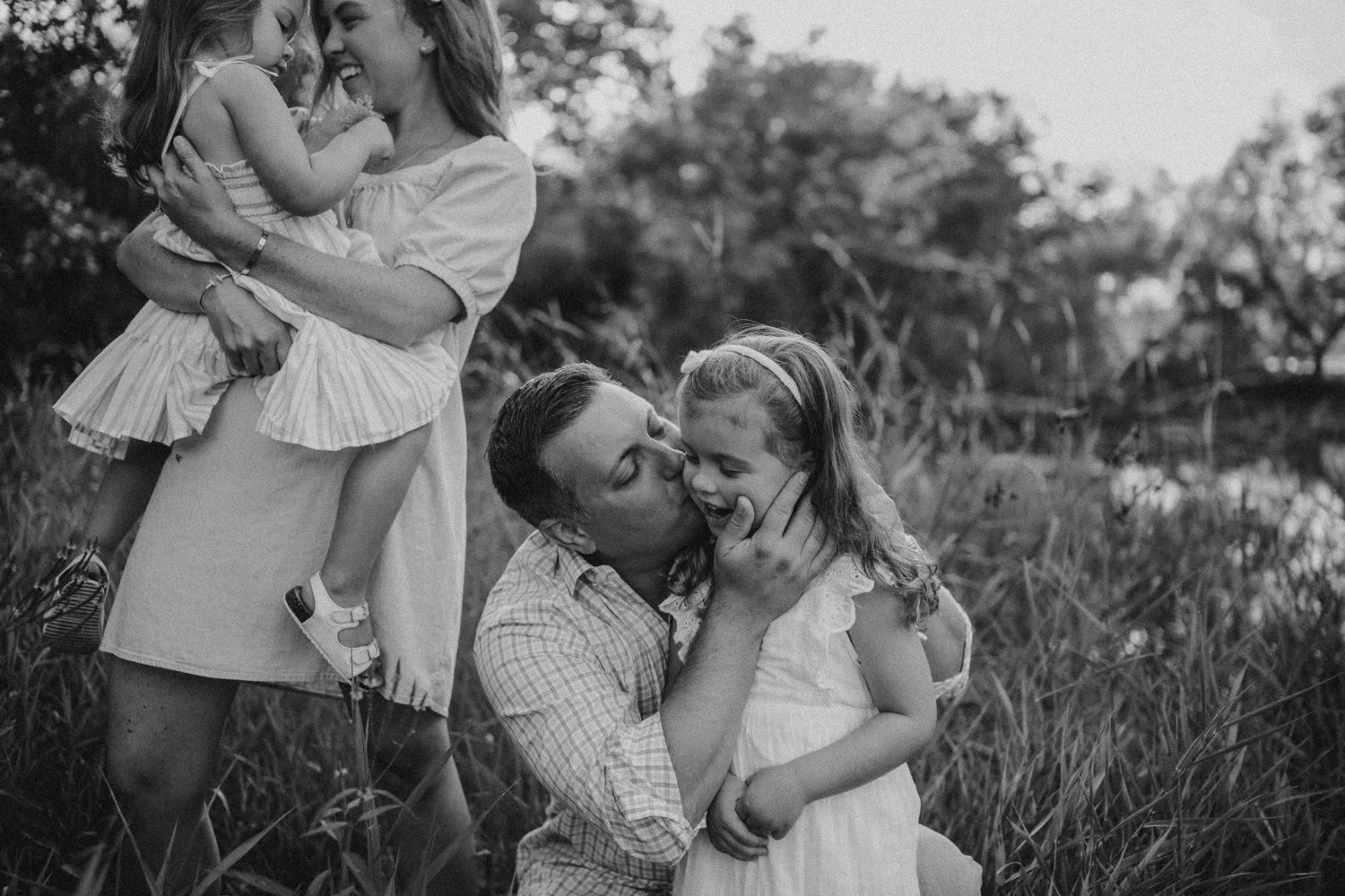 A black and white capture of a family sharing playful moments outdoors.