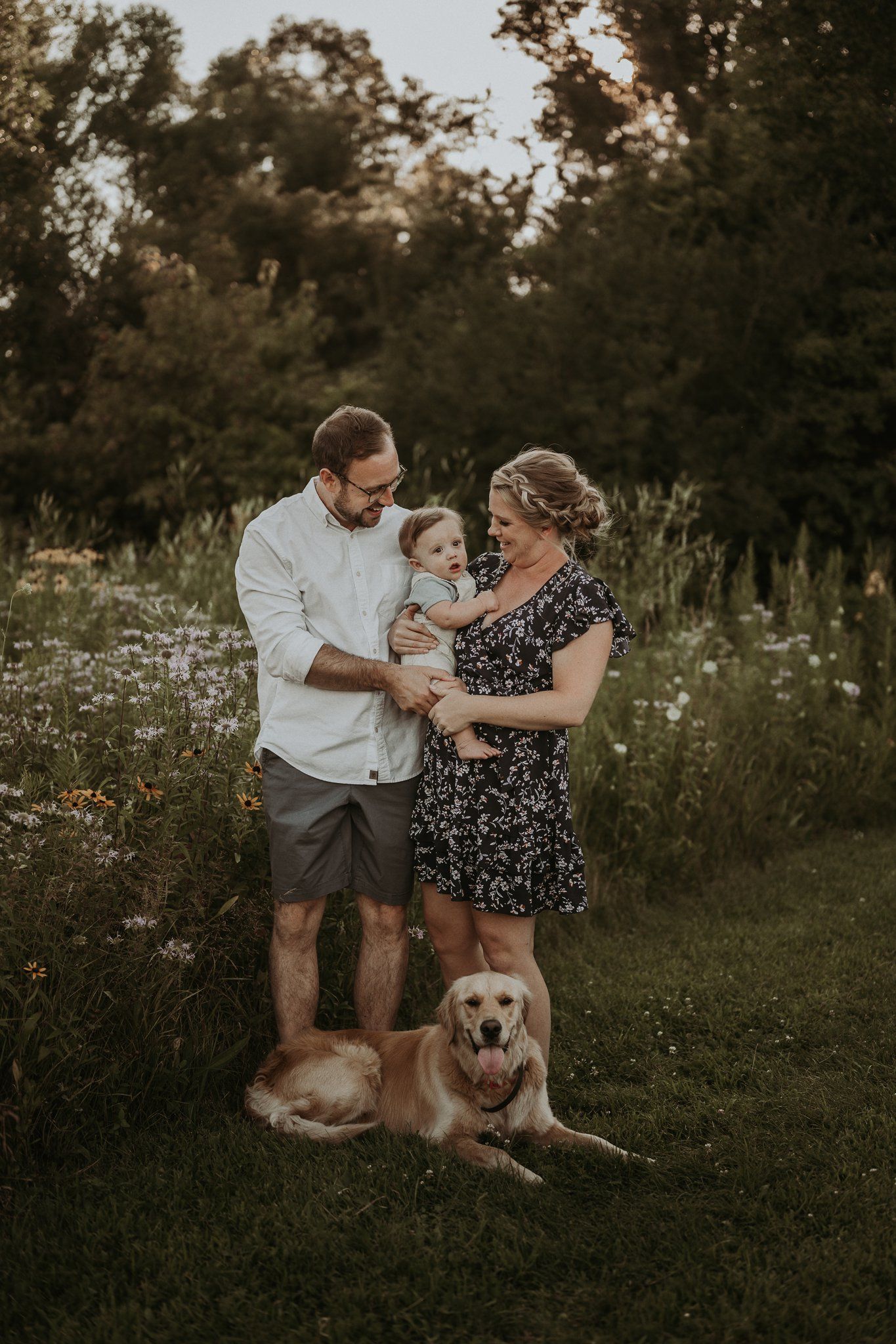 Family portrait in wildflower field with golden retriever dog at sunset.